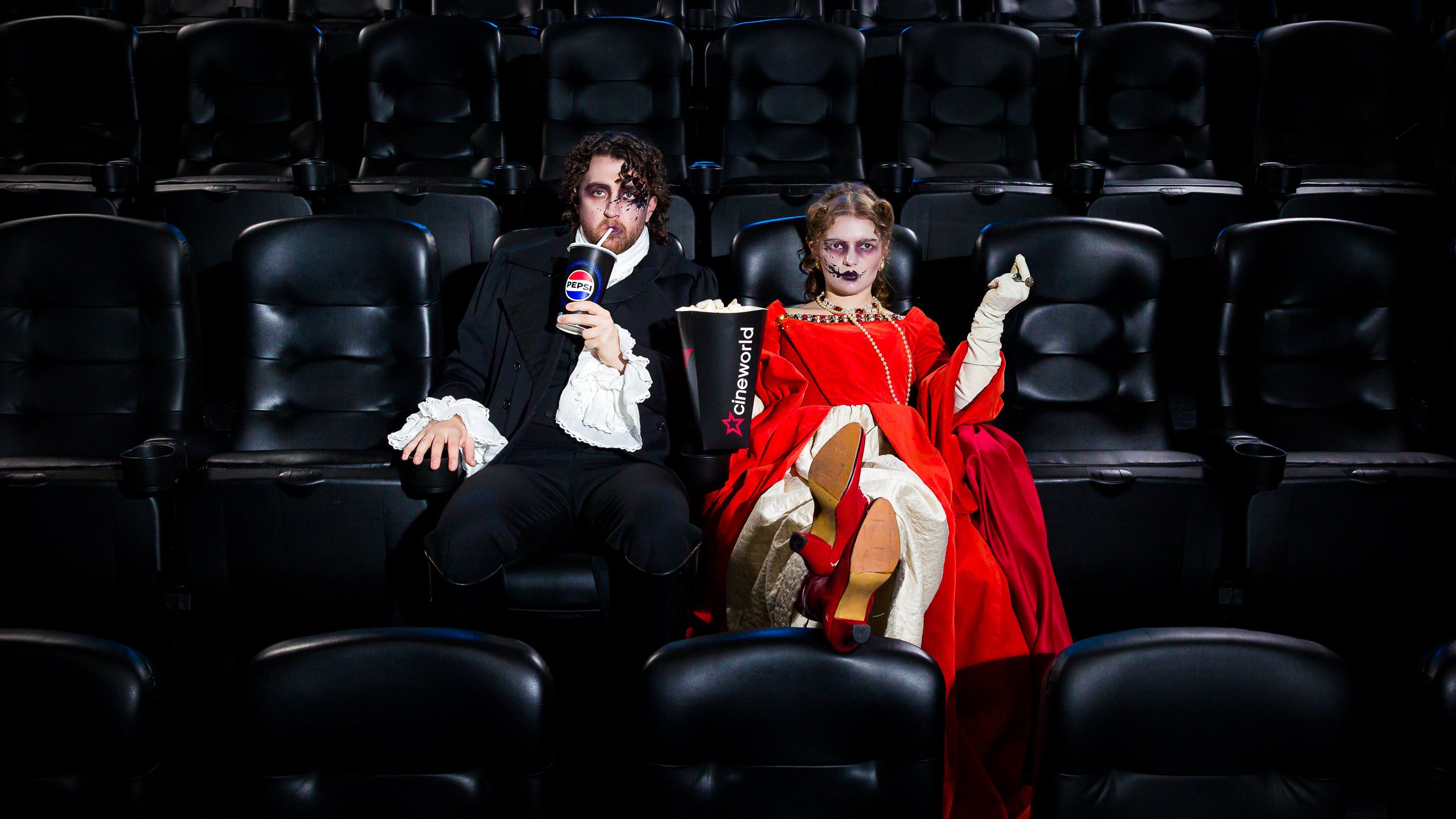 A man and woman in 18th century costume watching a film in the cinema
