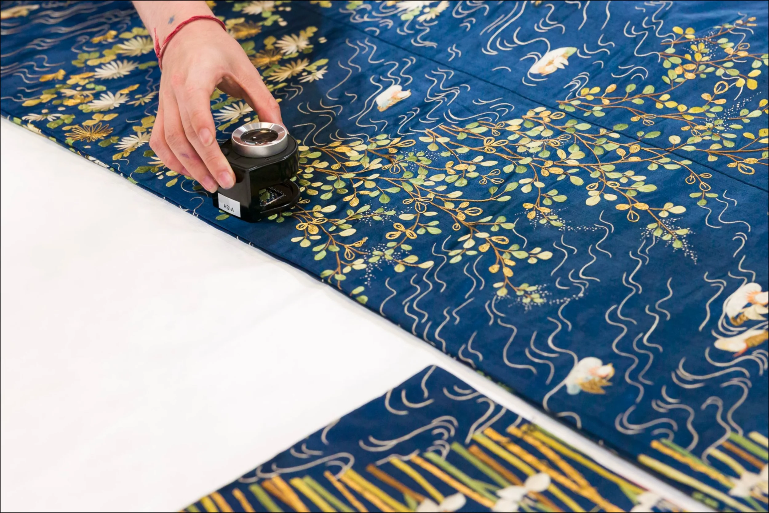 A hand holds a magnifying glass over the fabric of a kimono