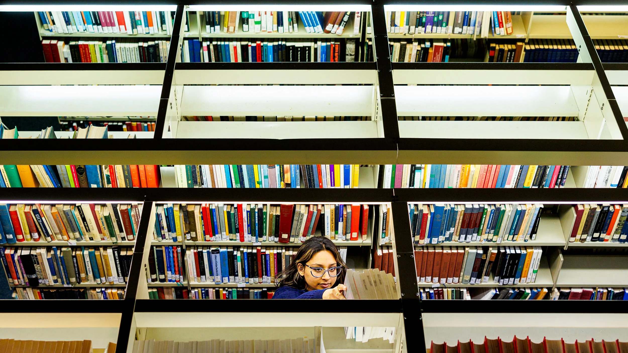A student reaches up for a book in a library