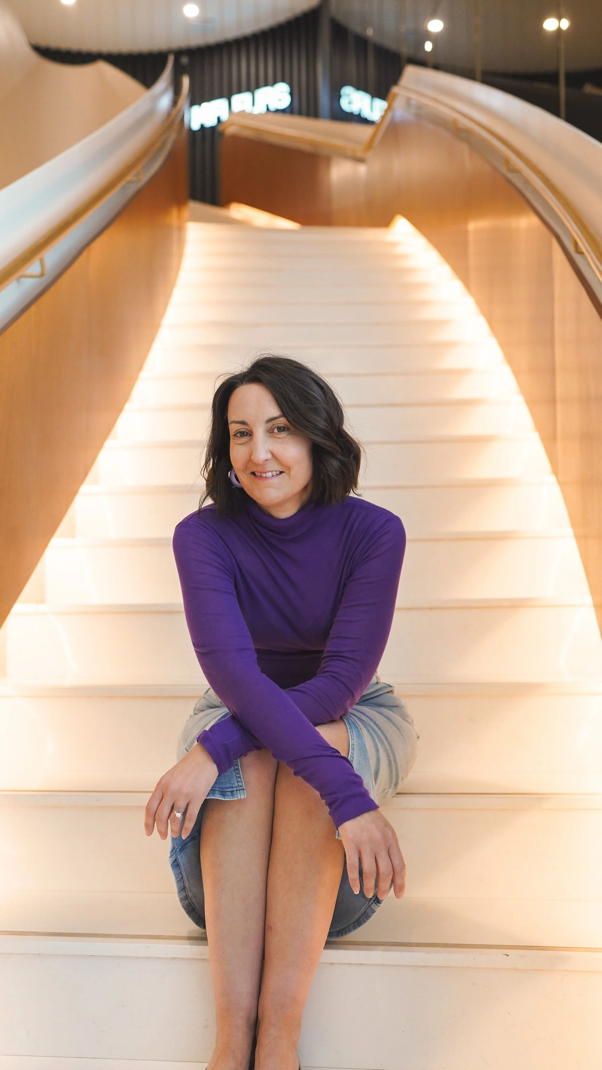 Portrait de Jaime assise dans un escalier moderne, en chandail mauve