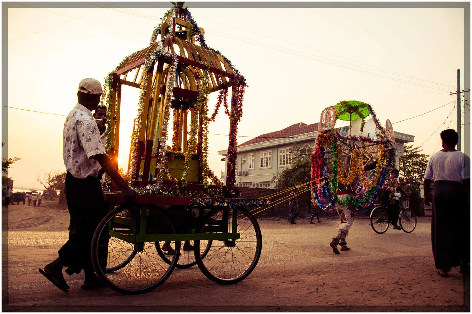 The devotee pulls the carriage down the road as the sun sets in Mawlamyine. © Dustin Main 2013