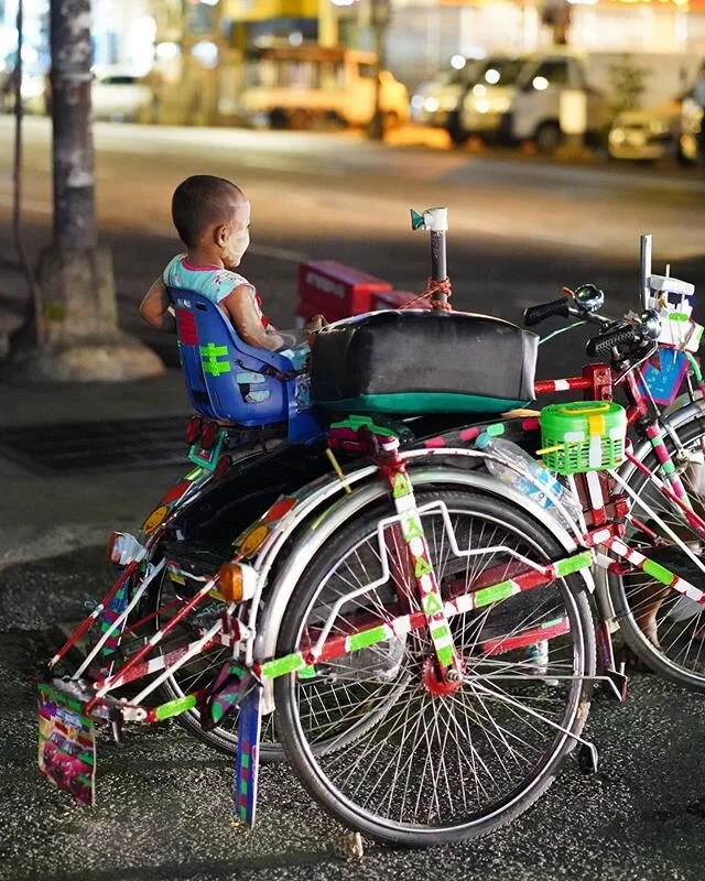 Baby on Board

The trishaw is a staple of Myanmar travel.  Take a ragged old bike, with only a single gear and tires worn so much that they constantly need repairing.  Then weld on a side car.  Toss a couple of cushions on there, and it's time to pick up the ladies from the market with their baskets full of veggies

At least that's how it has been.  Trishaws and their drivers once littered the streets of Yangon and other "non-hilly" cities and towns in Myanmar.  But with an influx of cars on the road in the past few years, they are all but banned from the streets here during the day.  At night, they come out again when the streets are less packed with traffic

This is the first and only time I've seen a baby seat attached to a trishaw, and the fact that it's such a colorful one is just an added bonus

Like many things changing so rapidly in Myanmar, this little one in the back seat might not remember a time when these 3-wheeled pedal-powered machines roamed the streets

#UnTourToMyanmar #ThisMyanmarLife #Myanmar #yangon #everydayasia #everydaymyanmar #burma #documentaryphotography #documentary #passionpassport #bbctravel #tbscommunity #myanmarigers #trishaw #pedalpowered