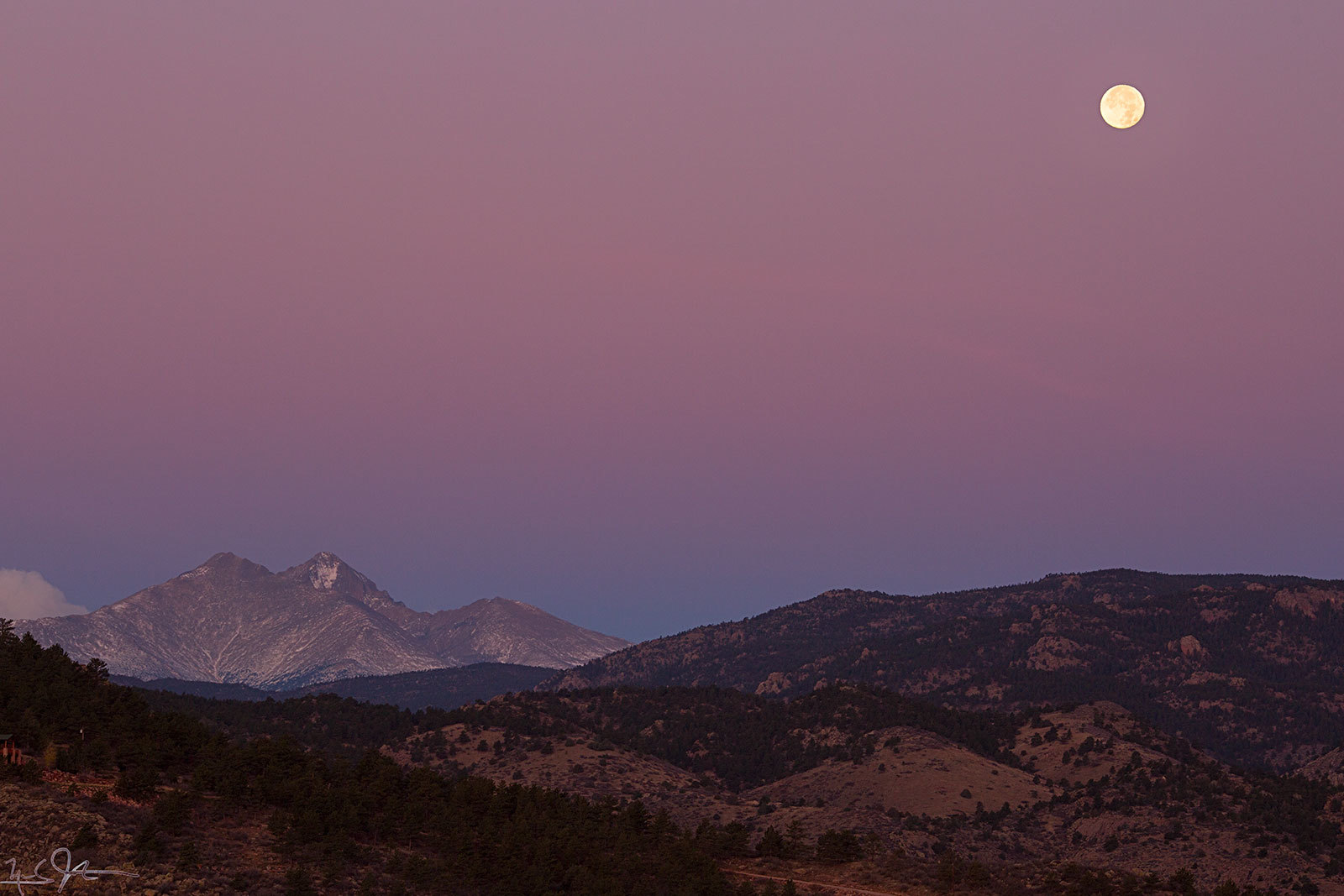 Purple alpenglow suffuses the horizon as the full moon sets just at sunrise.