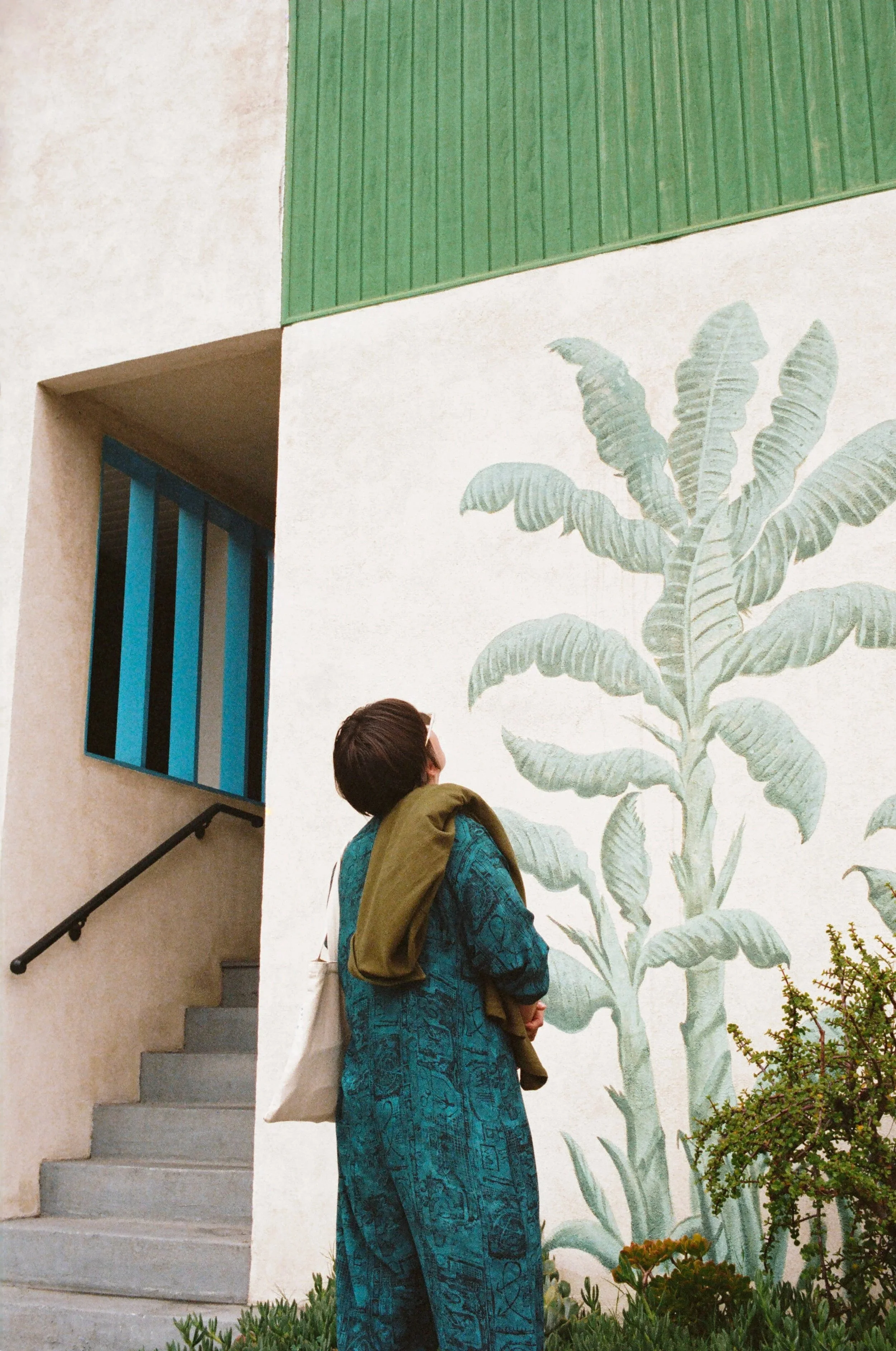 Person standing near a large mural of a banana plant on a white wall with green and blue accents.