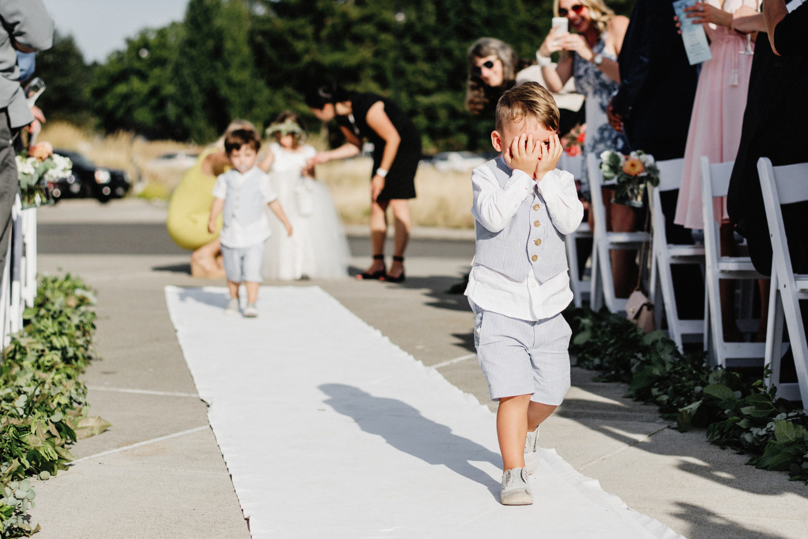 235-ring-bearer-hiding-while-walking-down-the-aisle-at-chambers-bay-in-tacoma.jpg