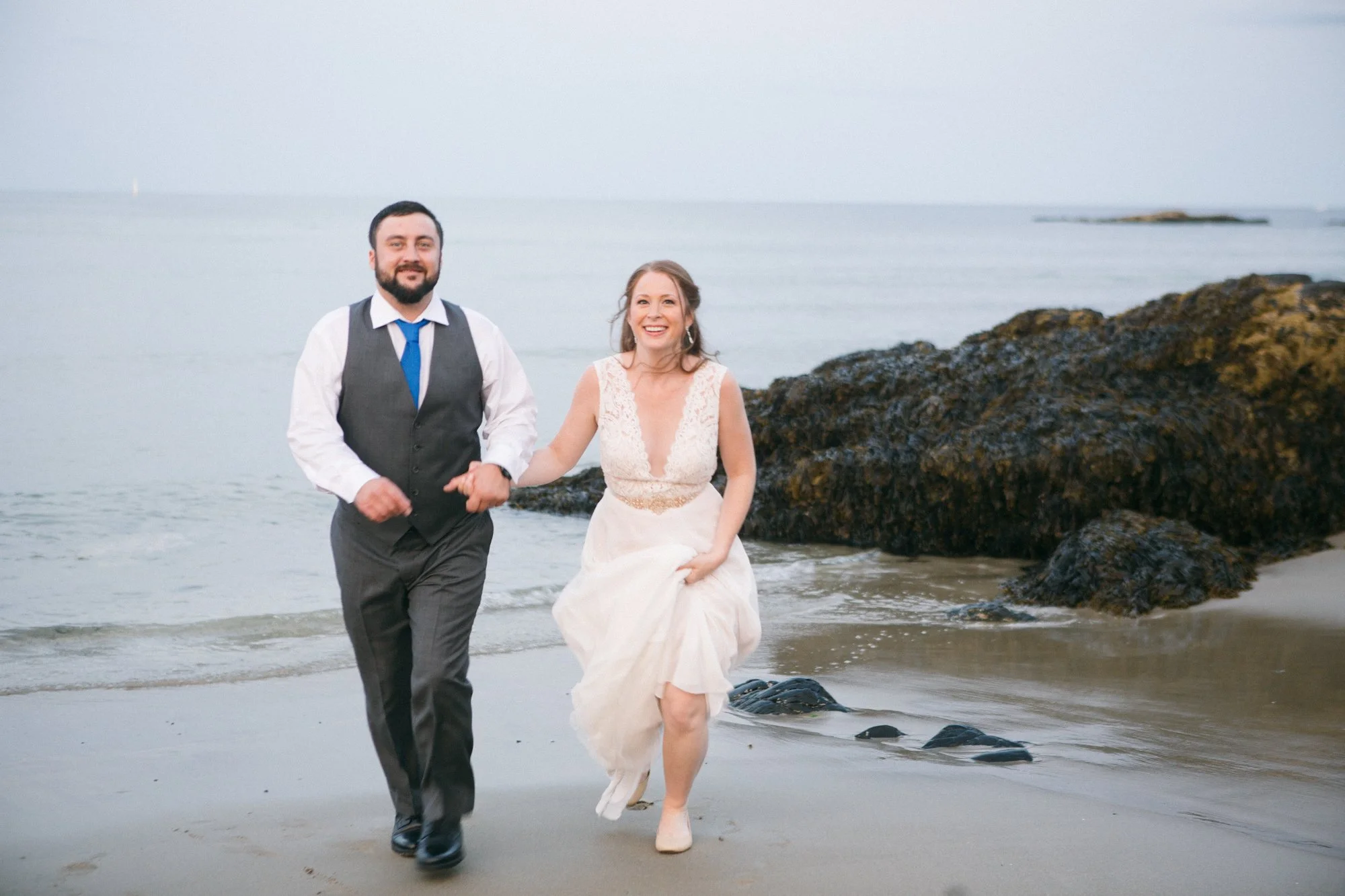 A couple run toward the camera on a rocky beach in Maine