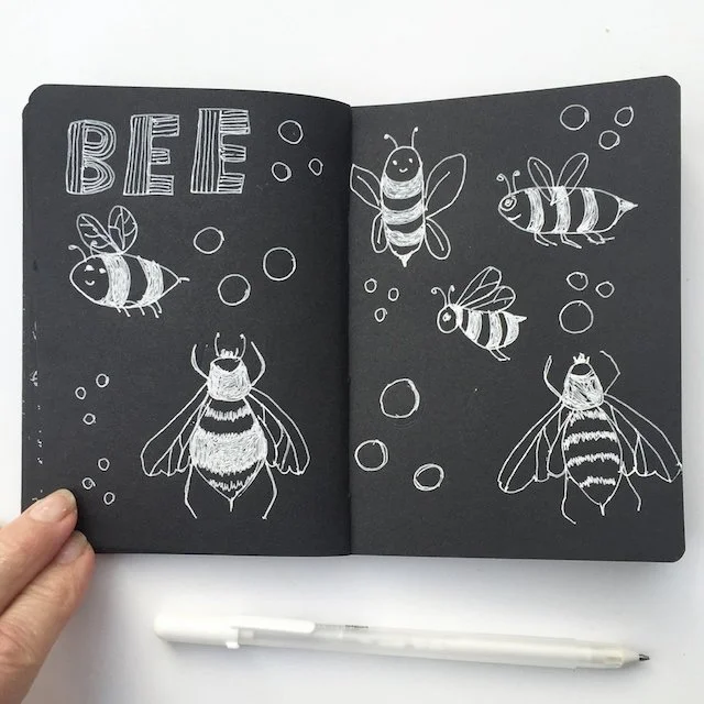 sketches of honey bees with white pen on black paper