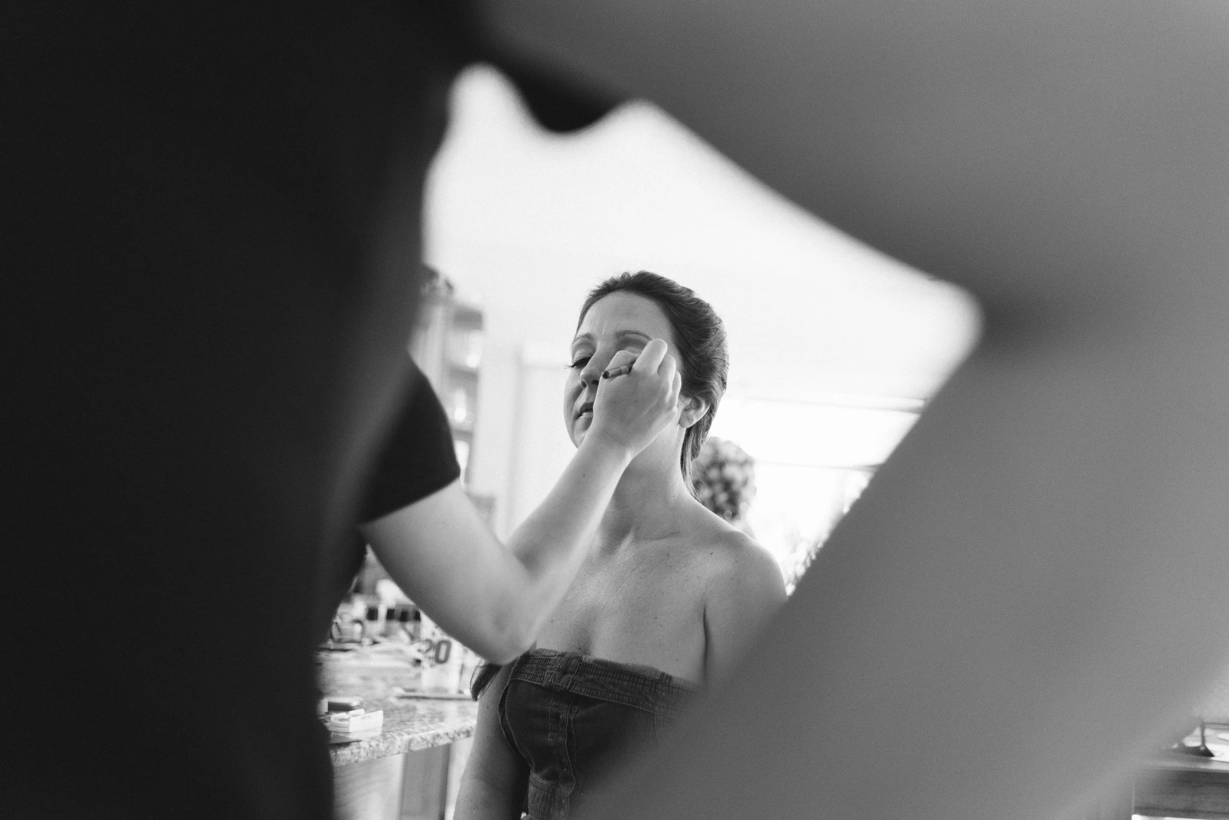 A woman sitting in front of a mirror getting her makeup done by an artist.