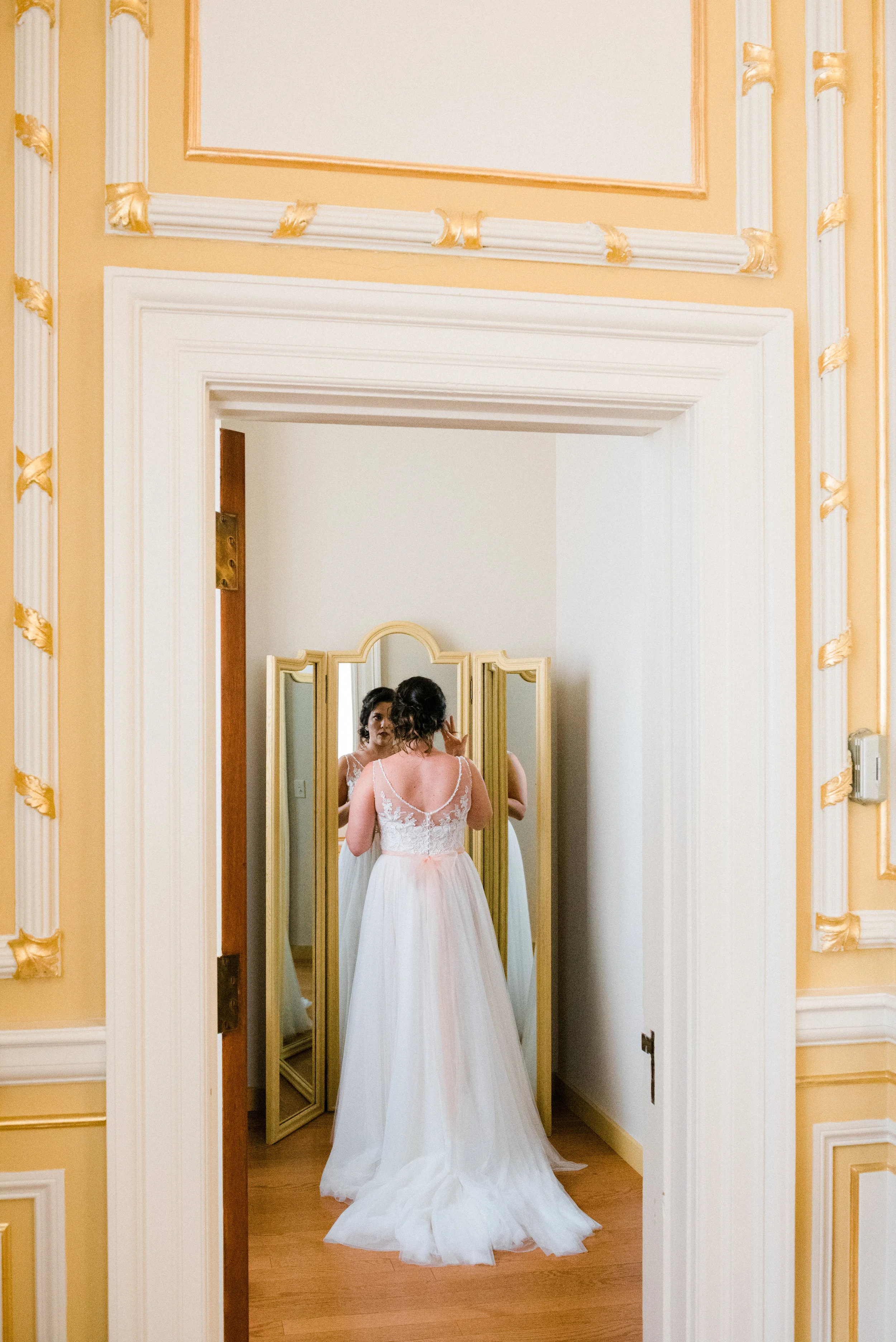 A woman in a wedding dress looking at herself in a mirror.