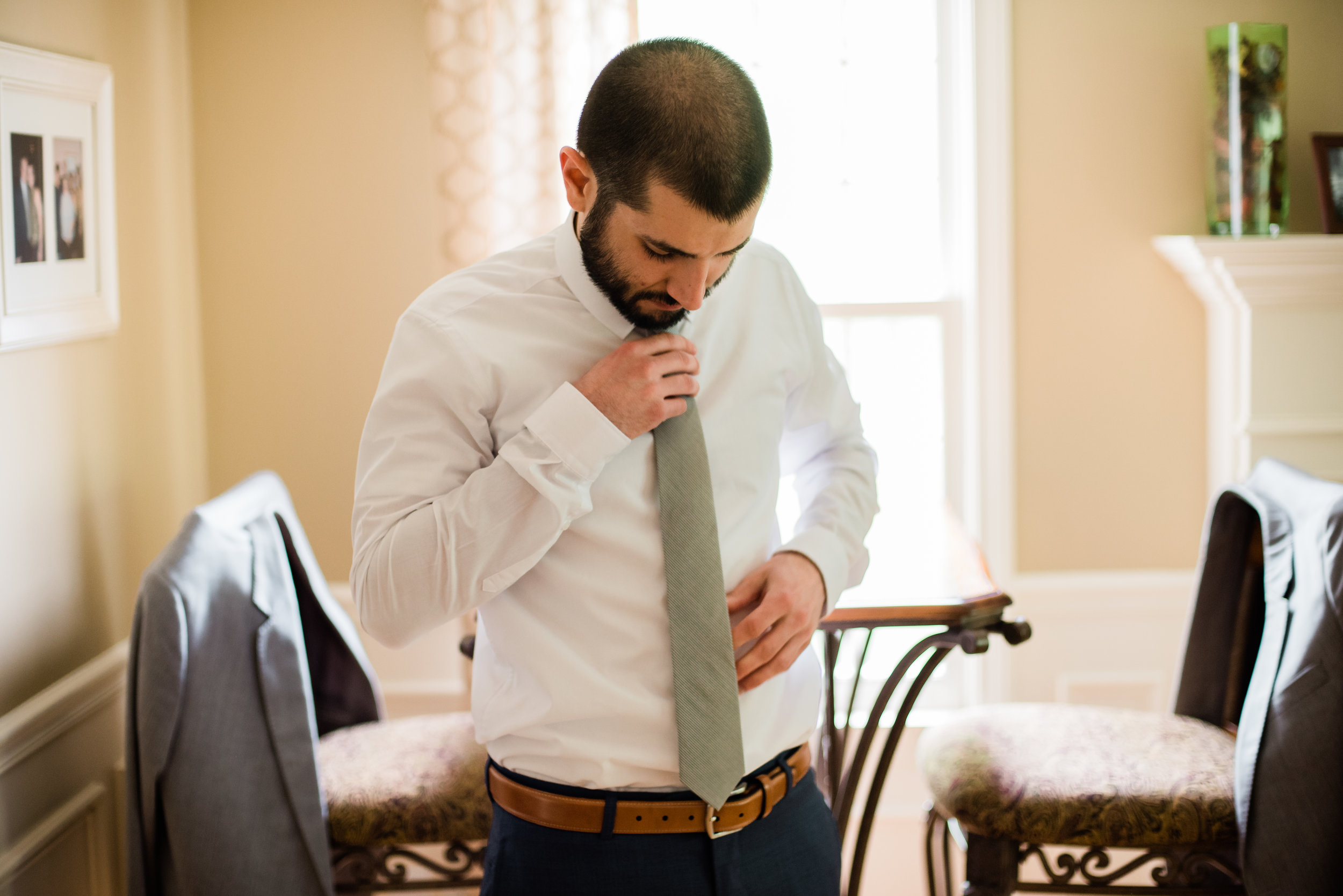 Man adjusting his tie in a dining room with chairs and a table.