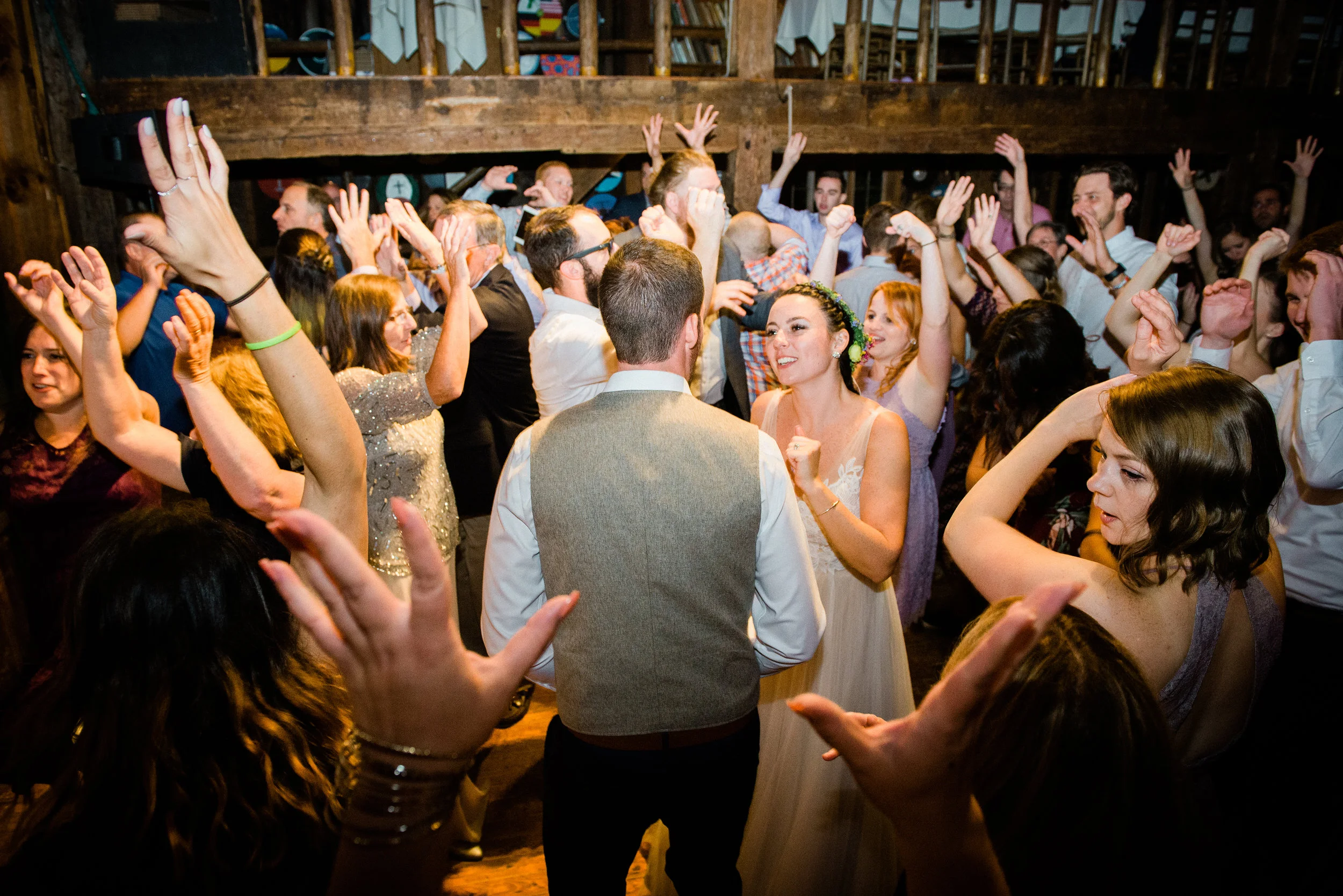 Crowd of people dancing at a wedding reception with a bride and groom in the center.
