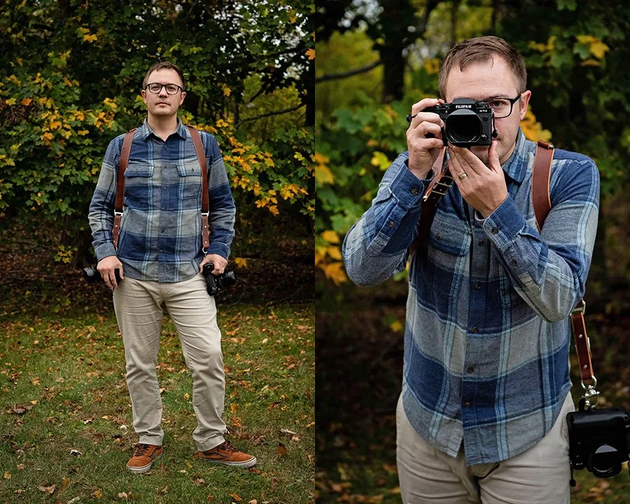 Man in plaid shirt holding camera outdoors in a wooded area