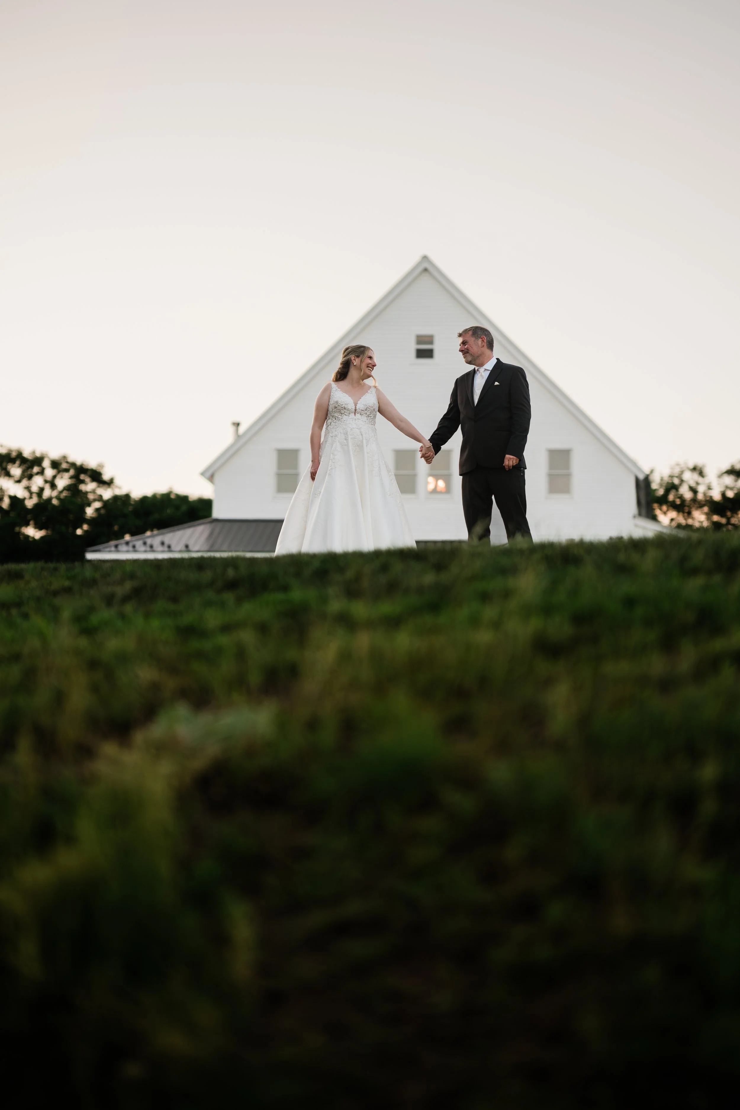 A bride and groom placed strategically in from of a building on a hill just after the sun had set during their wedding at Bear Mountain Inn + Barn in Main.