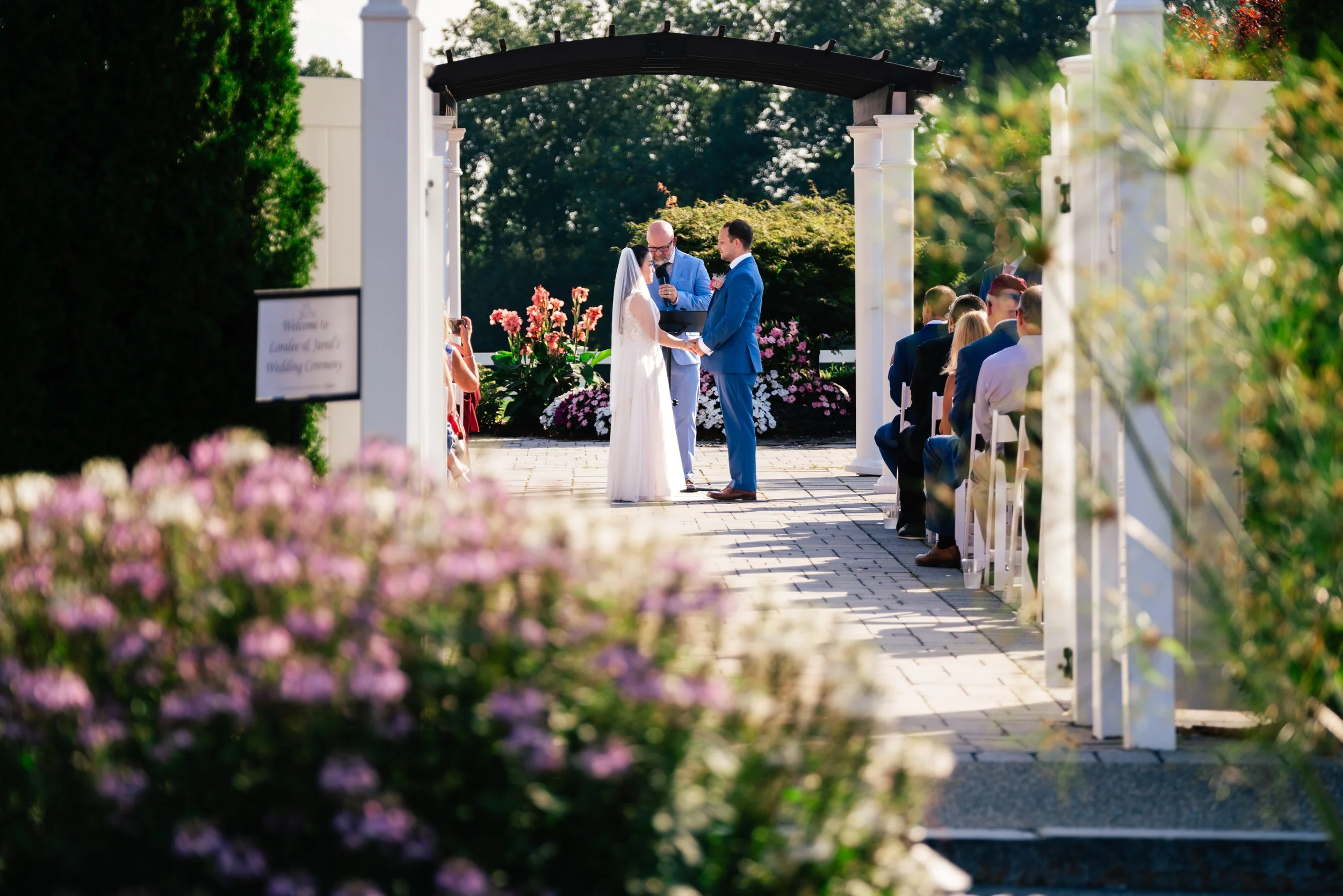 A bride and groom hold hands during their wedding at Four Oaks Country Club in Dracut, MA. Flowers decorate the grounds beautifully.