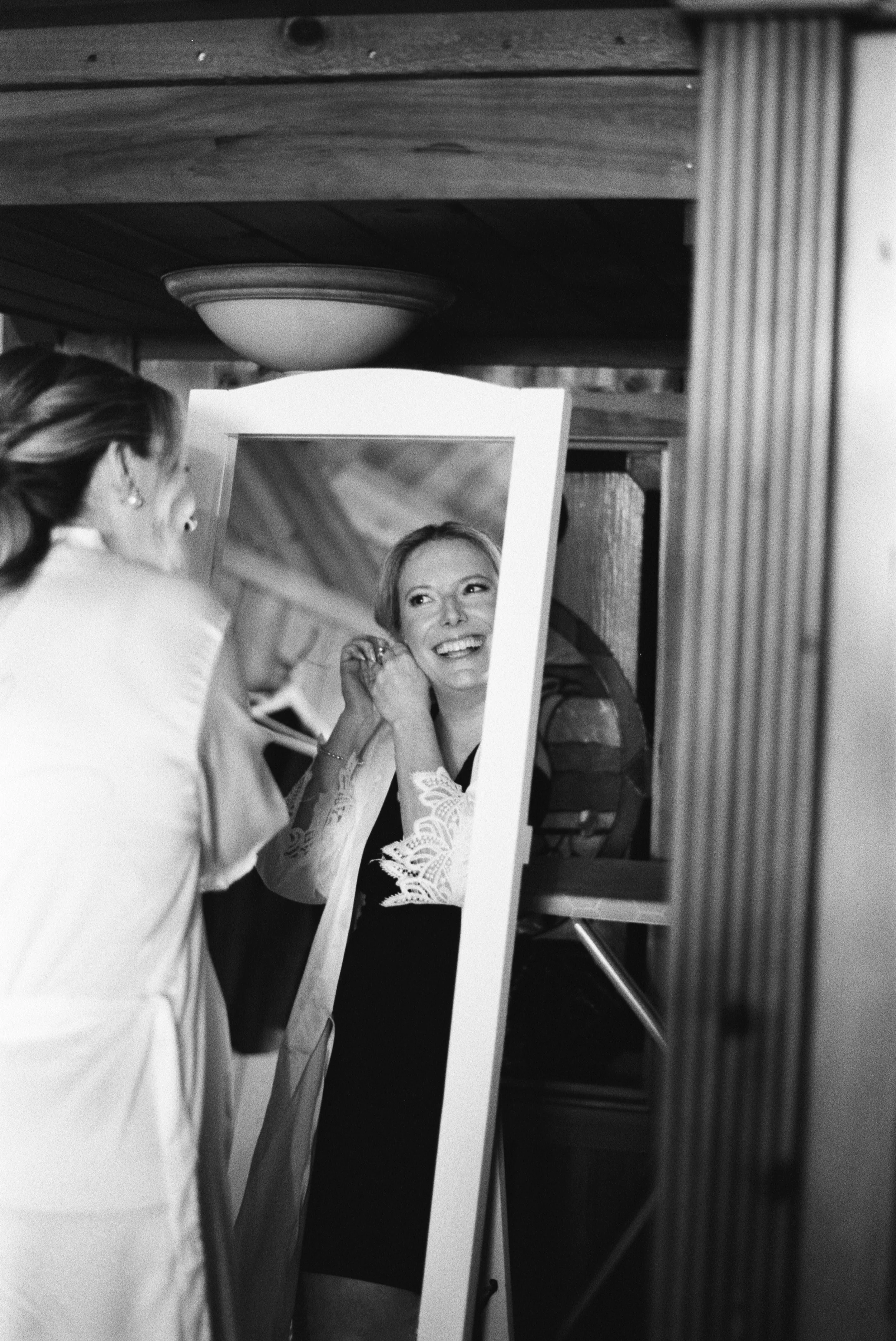 Black and white film photo of a bride looking in a mirror while getting ready for her Maine wedding.