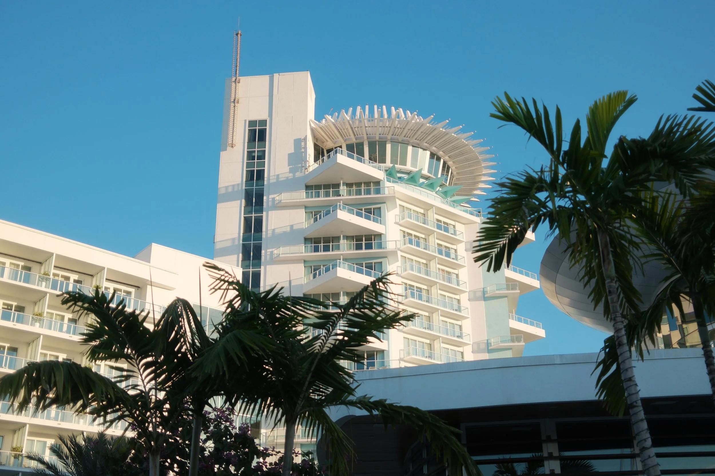 Pier Sixty-Six in Fort Lauderdale, Florida with balconies and a distinctive circular, rotating  bar/restaurant, surrounded by greenery and set against a clear blue sky.