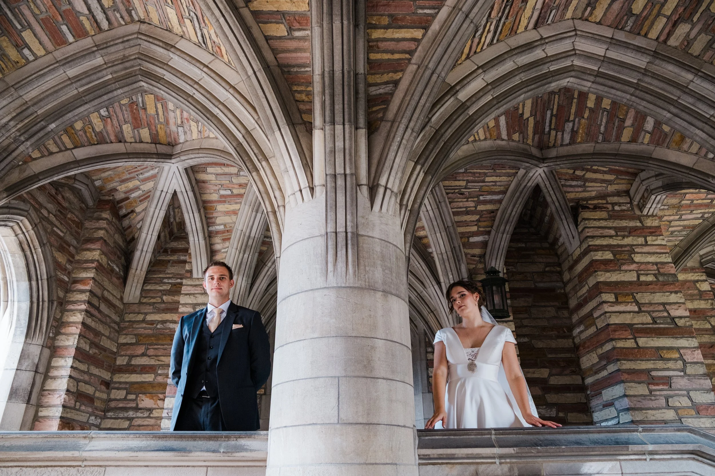 A groom and bride stand by a large pillar in a wedding portrait at the campus of Concordia Seminary St. Louis during their wedding in Missouri.