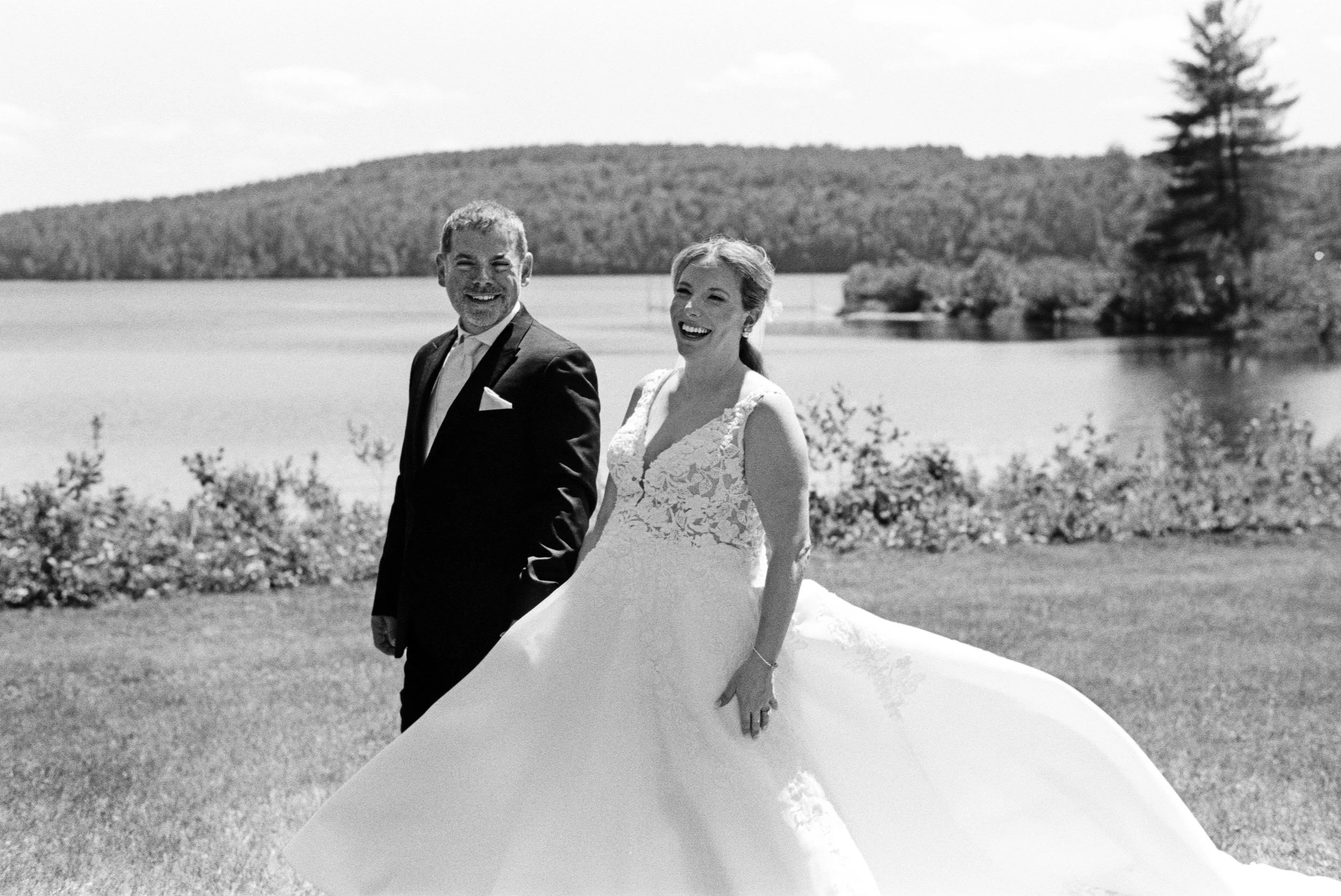 Black and white film photo of a groom and bride smiling by a lake during their Maine wedding.