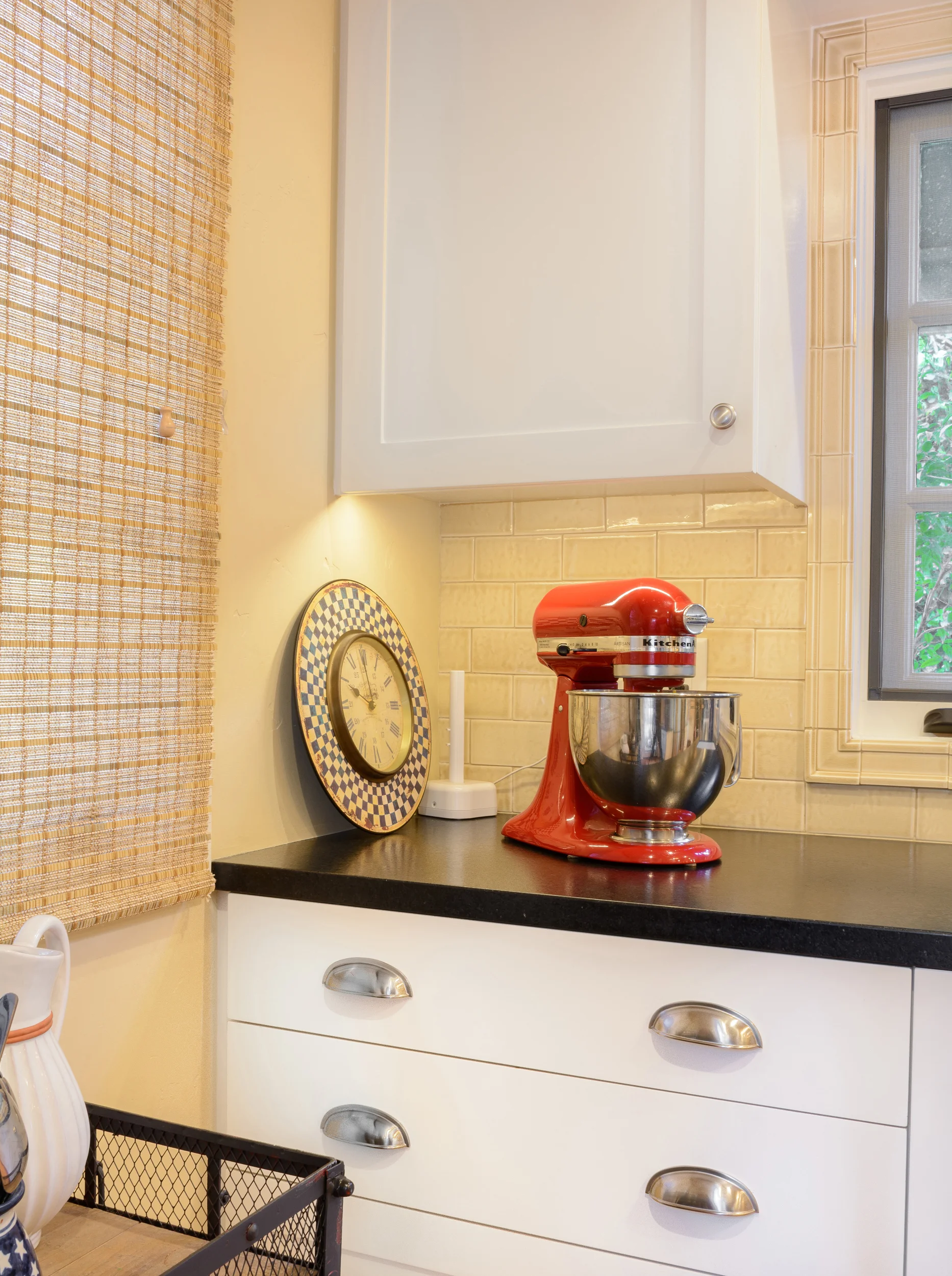 The red retro baking mixer and old clock add a hearty and colorful feel to the white Shaker cabinets with a black leathered stone top and tile backsplash