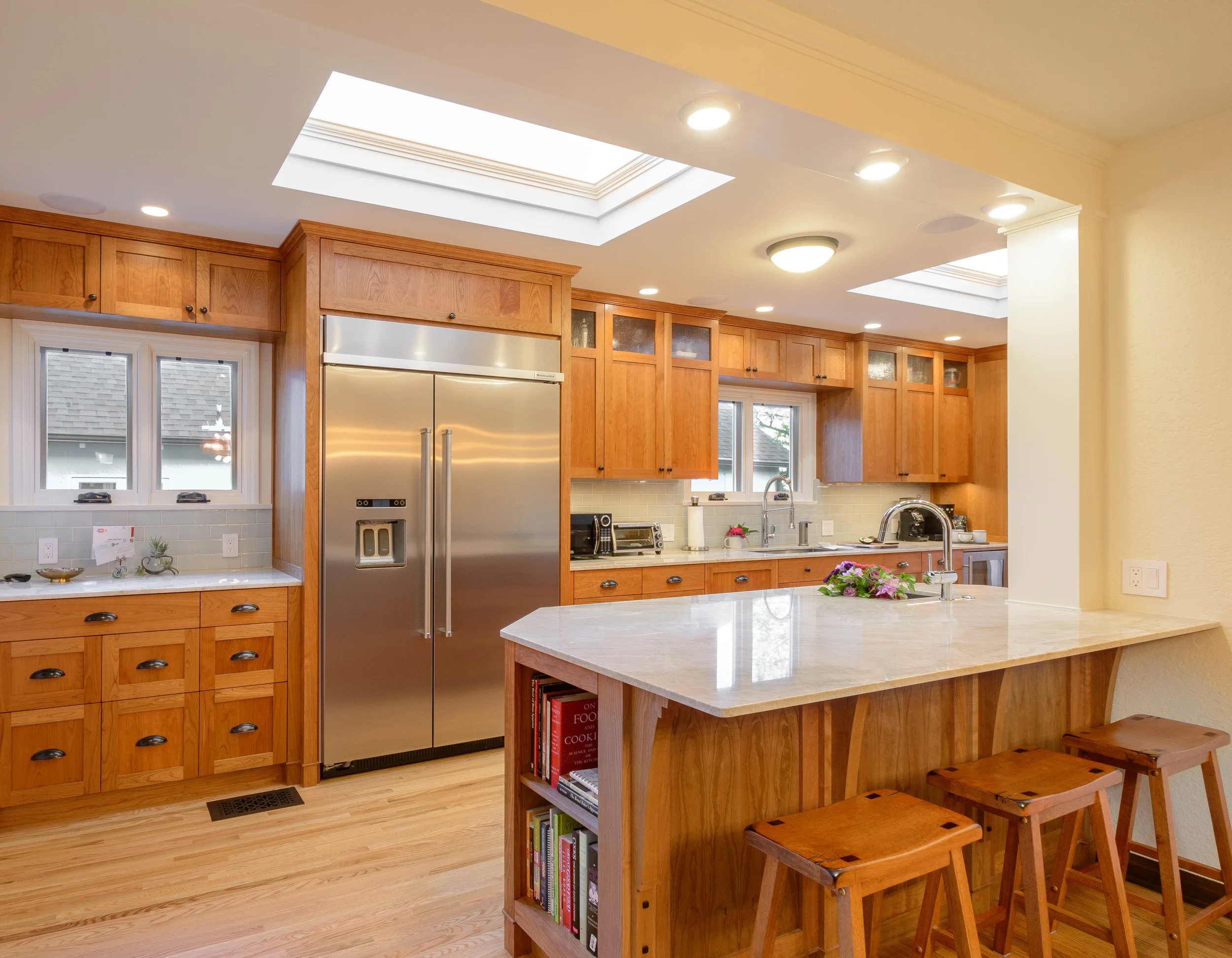 Impeccable lines and plenty of light for this Tudor kitchen remodel with custom-built cherry cabinets, accent hardware, oak floor, and a peninsula with a white stone countertop and bar seating area