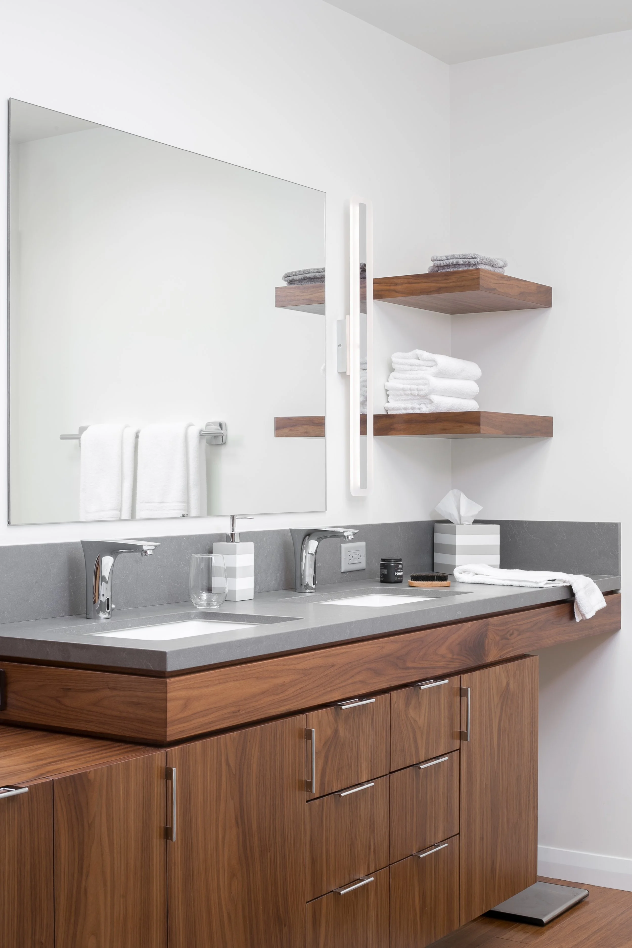 The minimalism and clean lines of the walnut cabinetry, large mirror and wall sconces combine perfectly warmth and modern design