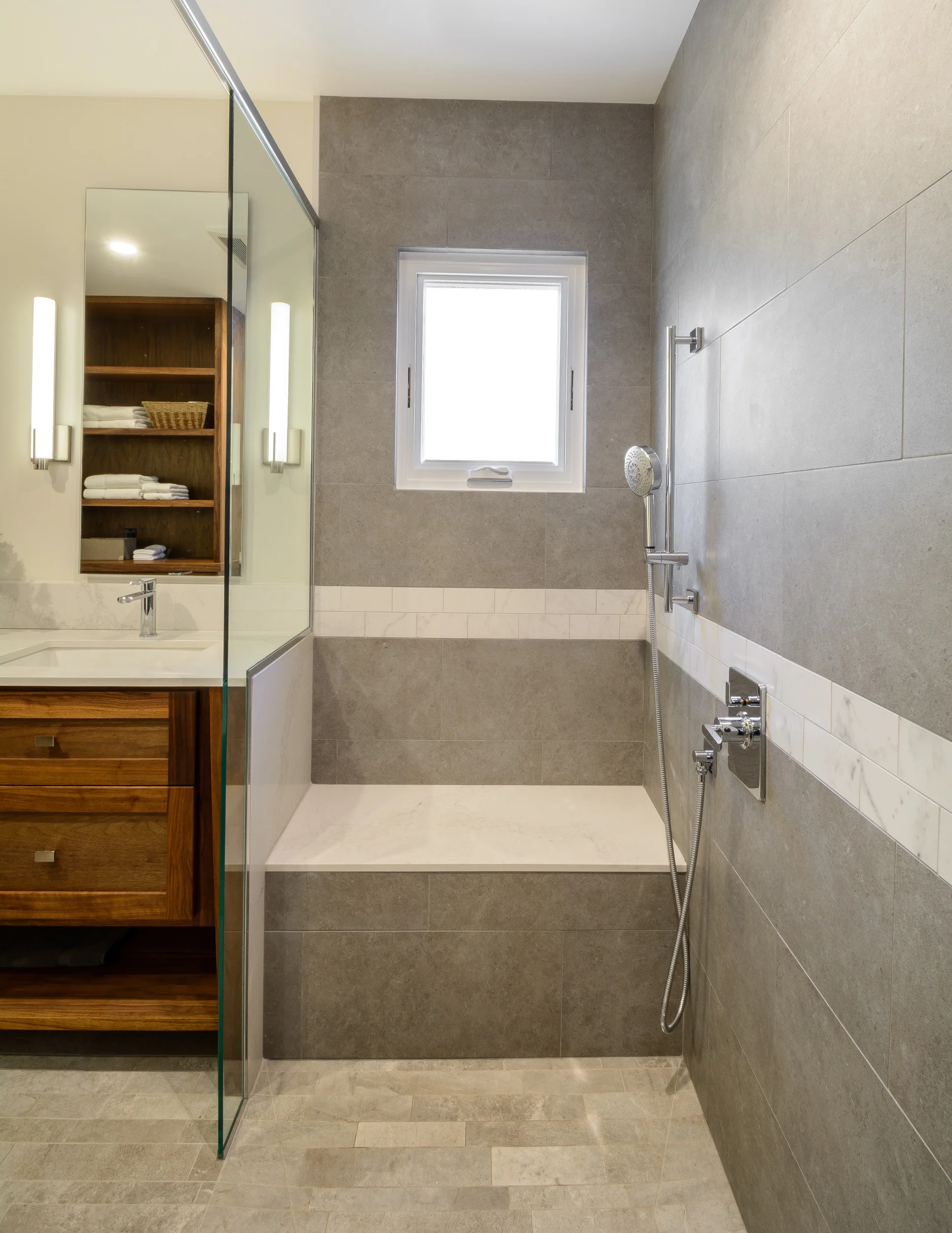 Shower seat with warming feature, small casement window for natural light, hand held shower fixture and custom walnut vanity