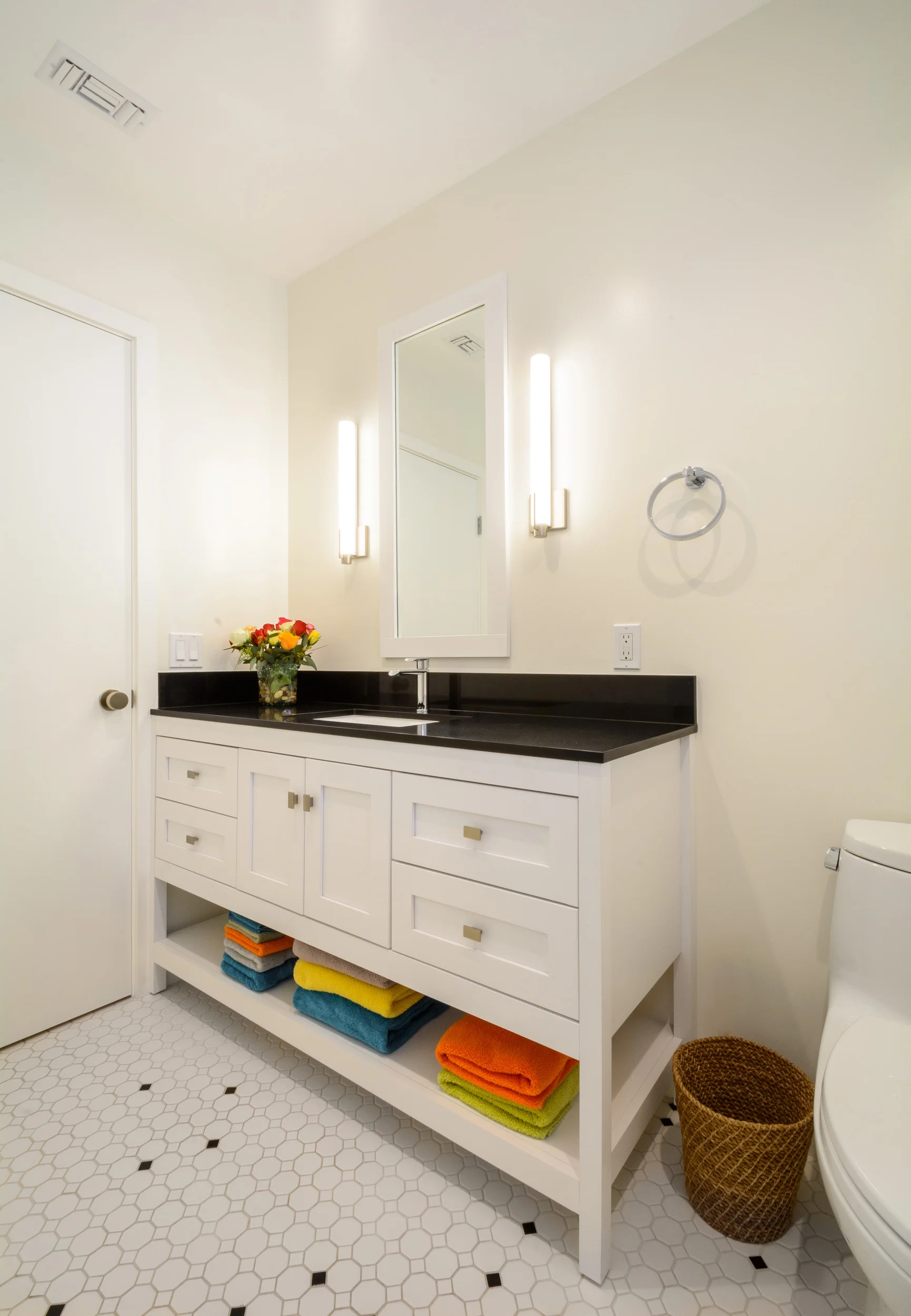White, black and a touch of color: this guest bath features a white vanity with an absolute black granite top and a floor of white octagon tiles and black dot accent tiles set in a unique pattern