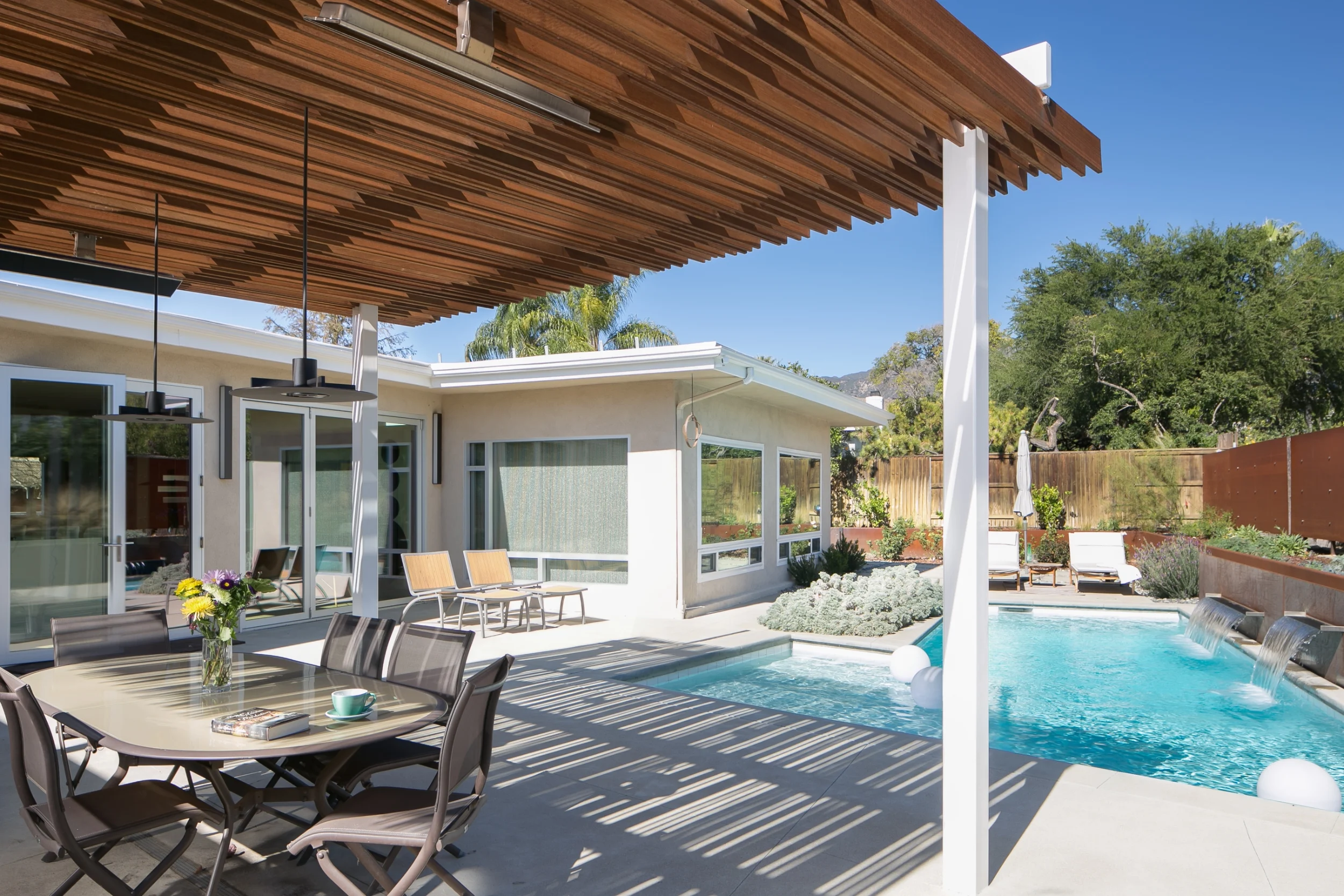 Mid-century modern backyard with water-wise landscaping, a pool accentuated with waterfall spillways off of a Corten steel wall, and a pergola for outdoor dining