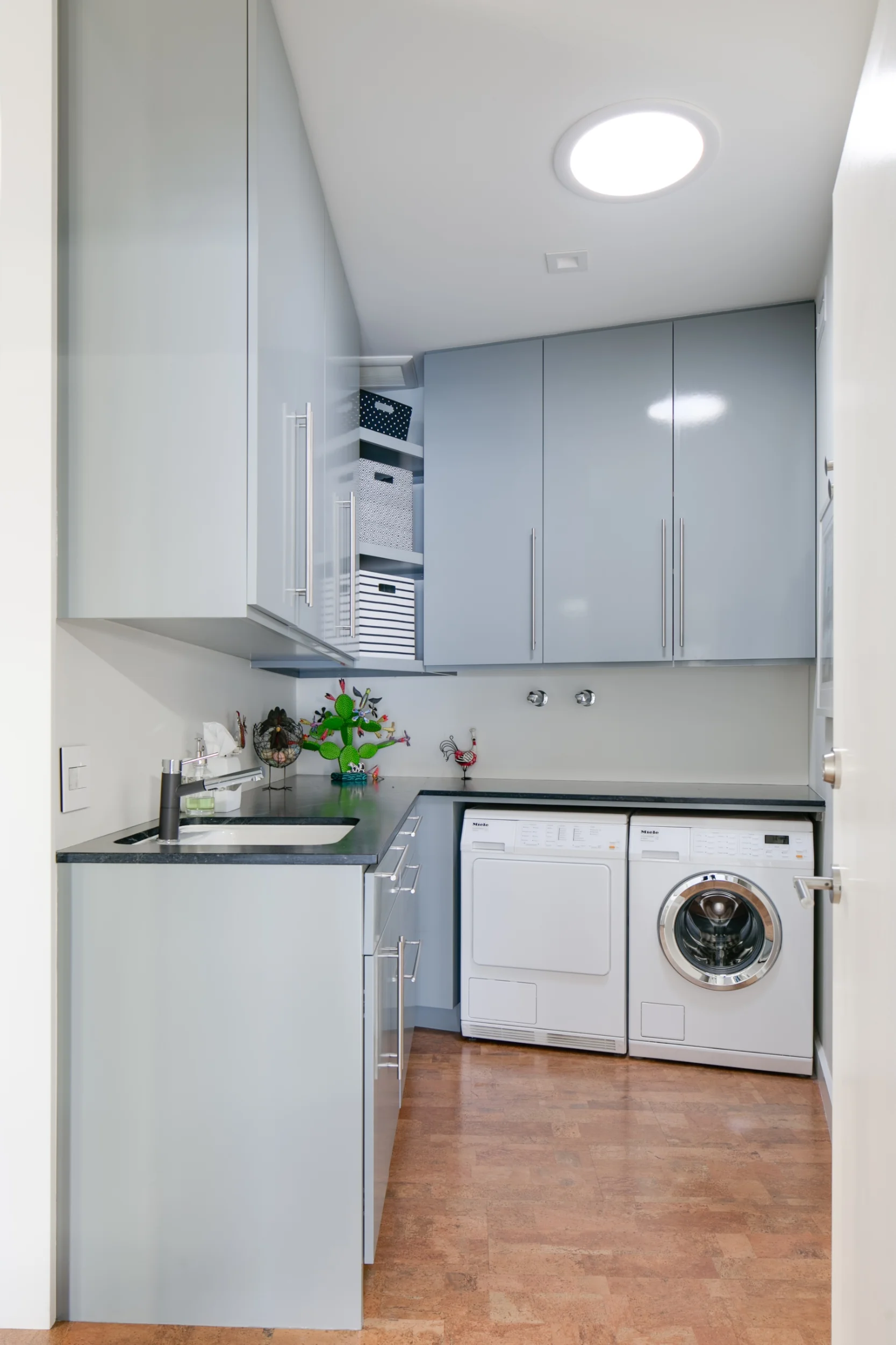 Mid-century modern laundry room with sleek gray cabinets, black quartz countertops and cork floor