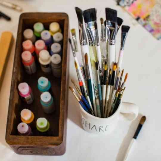 Paint bottles in a wood box and paint brushes in a mug