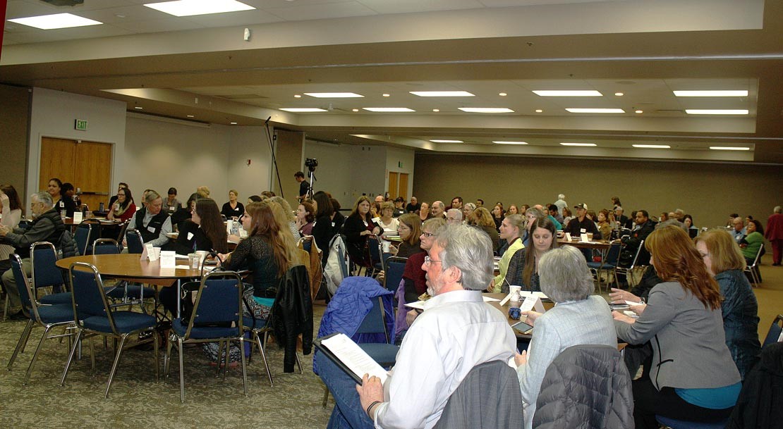 Attendees at the program “Building a Healthier Community” at the Linn County Fair and Expo Center Jan. 25th. The forum, from 10:00 to 2:00, featured talks by state and community health experts and leaders in affordable housing from Linn, Lincoln, and Benton counties. The goal was to show the intimate relationship between adequate housing and health, stressing the importance of integrating services to achieve both. Wearing a long-sleeved white shirt and seated at the table in front, almost in center, is Jim Moorefield, director of Willamette Neighborhood Housing Services.