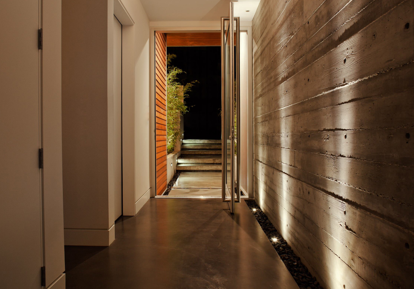 A beautiful example of a feature wall. The board formed concrete makes a bold statement. The material is very textural, spiking curiosity and asking to be touched. The wall is pulled away from the floor and separated by stones. While the floor is also concrete, the wall is distinctly different. The up lighting highlights the wall and further emphasizes its significance.