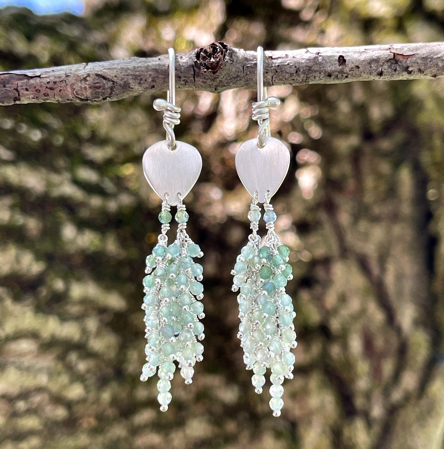 A pair of silver dangle earrings with dark to light teal blue clusters of indicolite tourmaline gemstone beads.