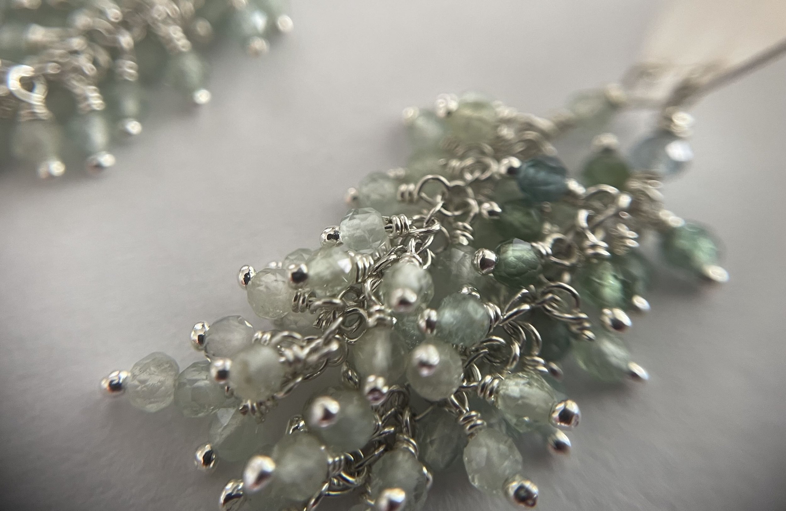 Detail view of A pair of silver dangle earrings with dark to light teal blue clusters of indicolite tourmaline gemstone beads.