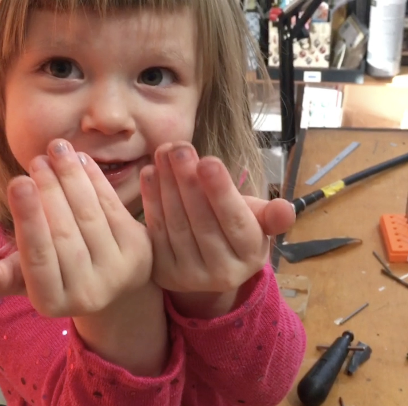 Young child in a jewelry studio, holding hands near her face with a curious expression.
