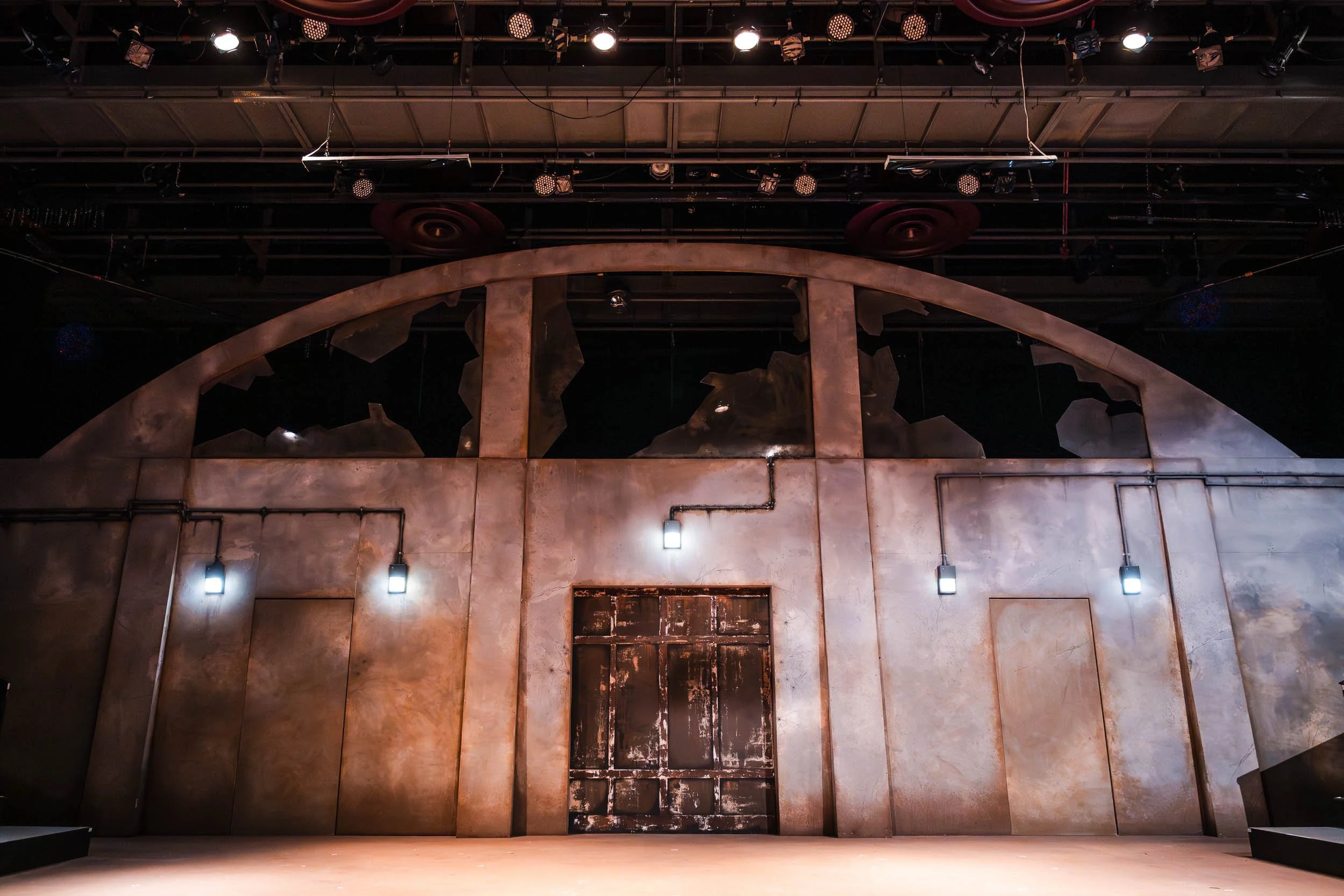 Black-box theatre stage set photographed during a university production of Antigone, showing the architectural set design and stage lighting before the actors enter the scene.