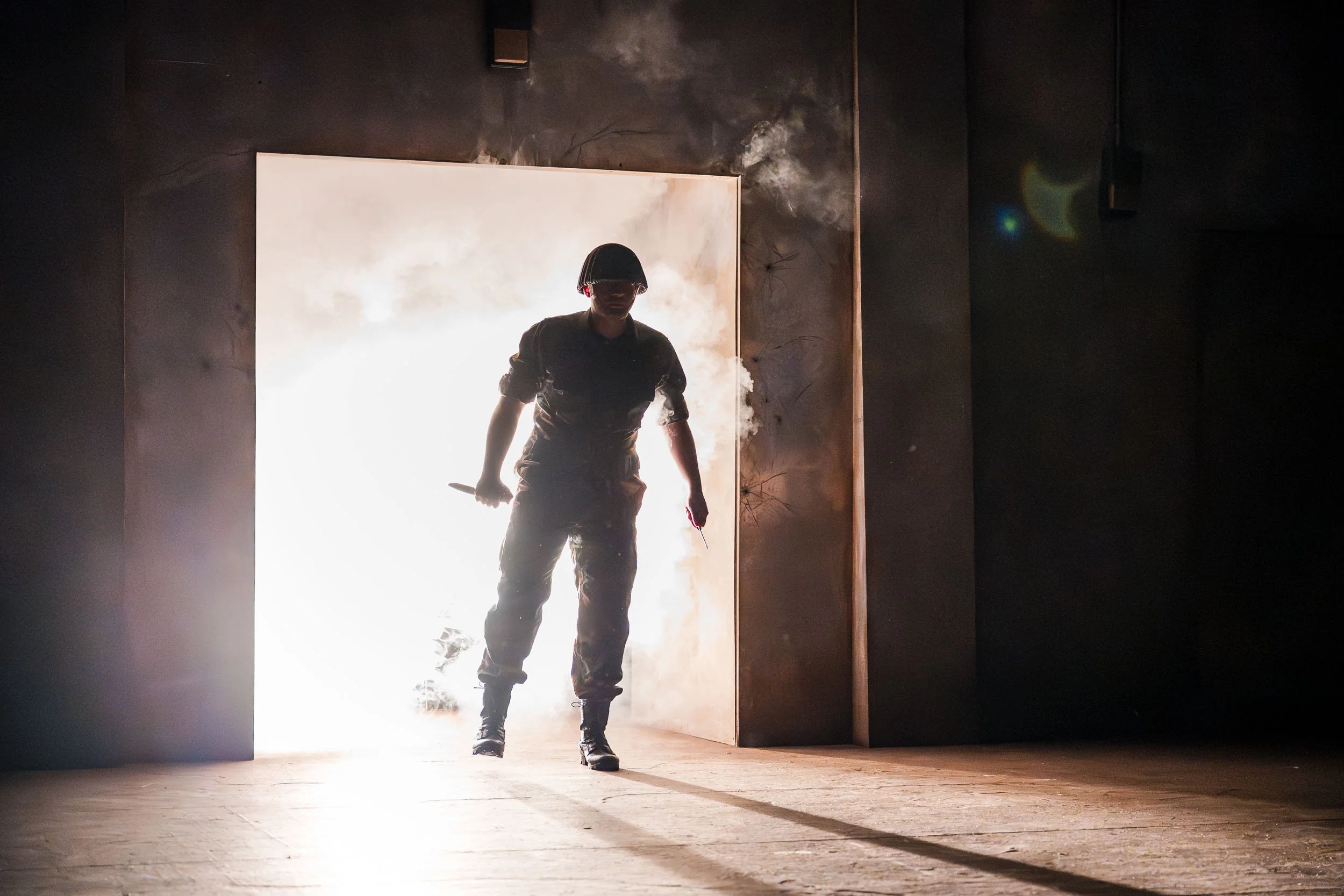 Actor entering through a brightly backlit doorway during a university production of Antigone, creating a dramatic silhouette against the stage lighting.