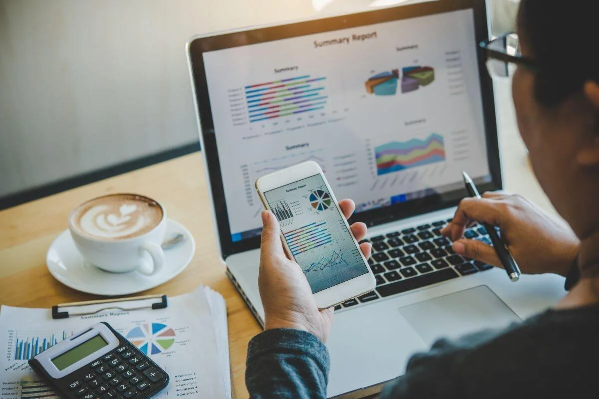Businessman using a laptop and smartphone to cross-check company cash flow reports, ensuring accuracy and financial oversight.