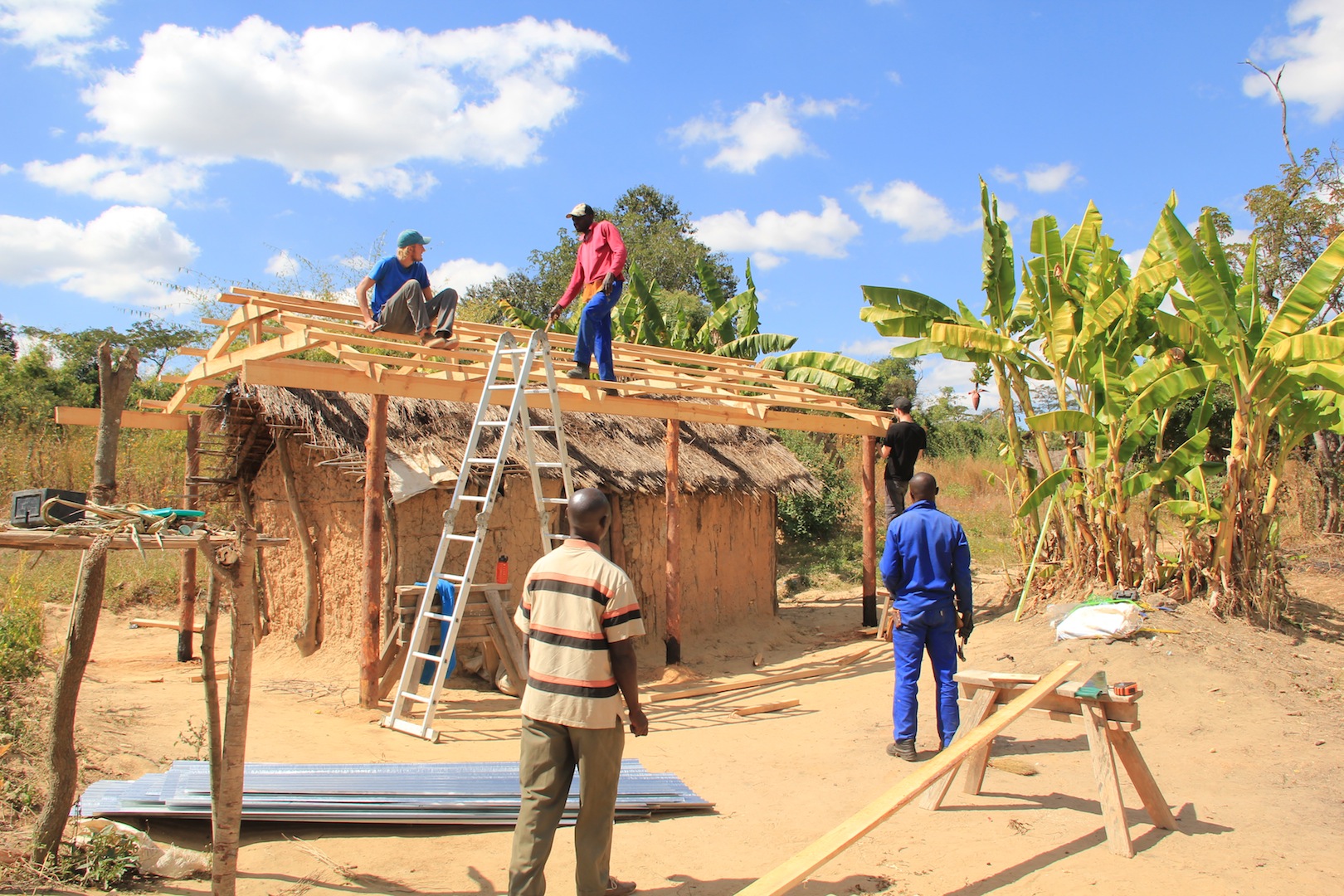 Devon in Zambia (sitting on the roof). Devon supported the Regional Support Team through maintenance and community home repairs with our visiting teams.