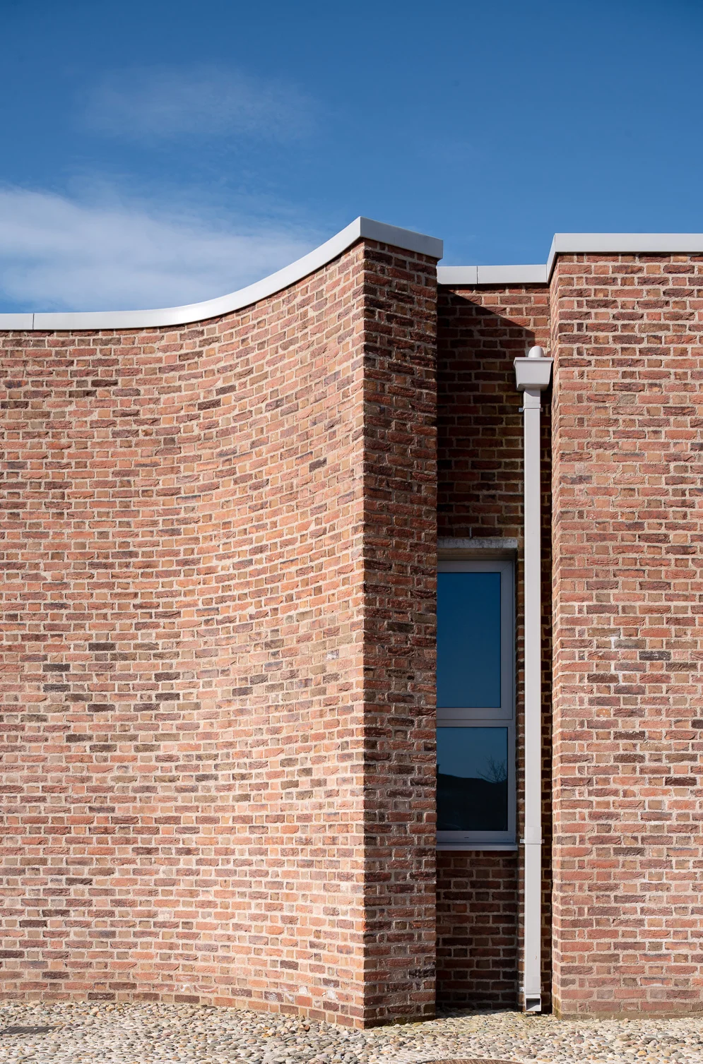 Curving handmade brick facade using a lime mortar and a flemish bon, with a local cobble groundscape.