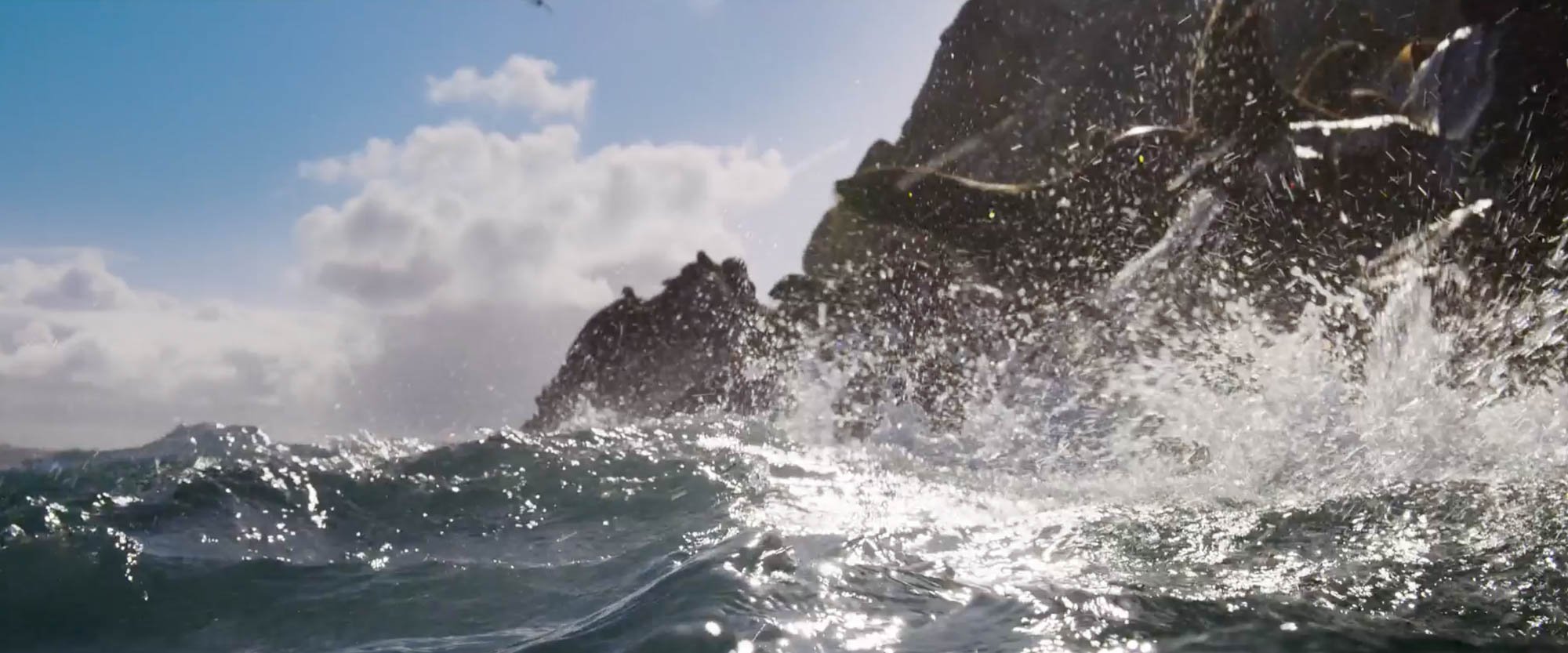 Ocean waves crashing against rocky cliffs with water spray and a partly cloudy sky