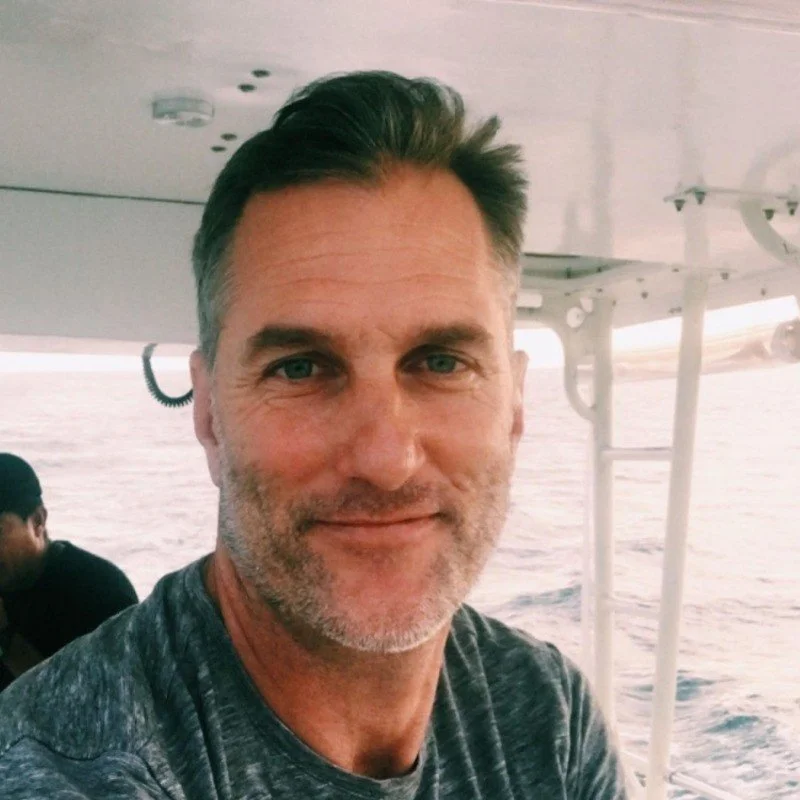 A middle-aged man with short dark hair and a beard, smiling on a boat at sea.