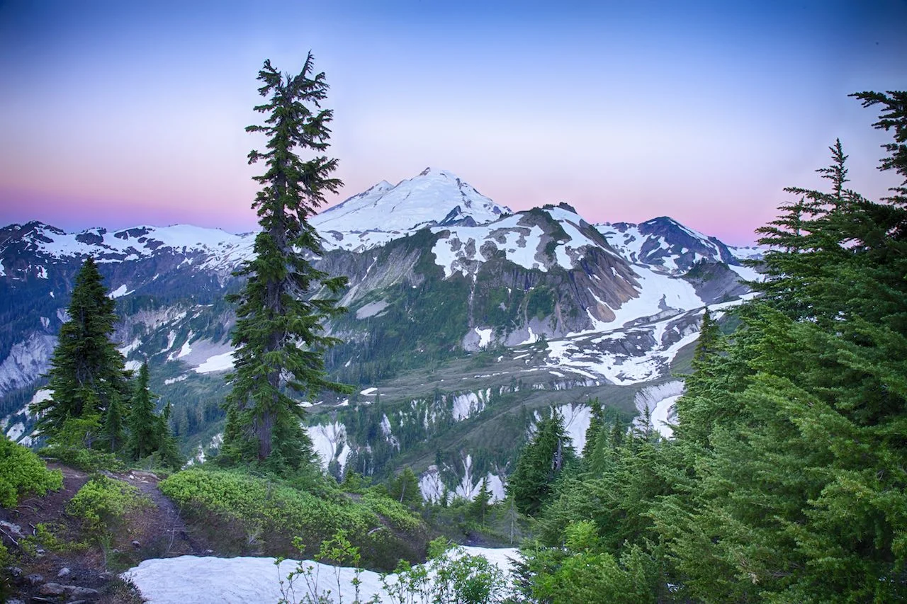 The first rays of the sun light up the sky around the peak of Mount Baker.