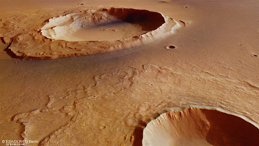 The background crater in Kasei Valles shows debris downstream from an ancient flood while the foreground crater shows signs of impact splashes. Credit: ESA/DLR/FU Berlin CC BY-SA 3.0 IGO
