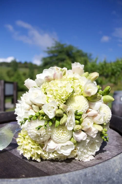White wedding bouquet of roses & carnations with greens and buds on outdoor table