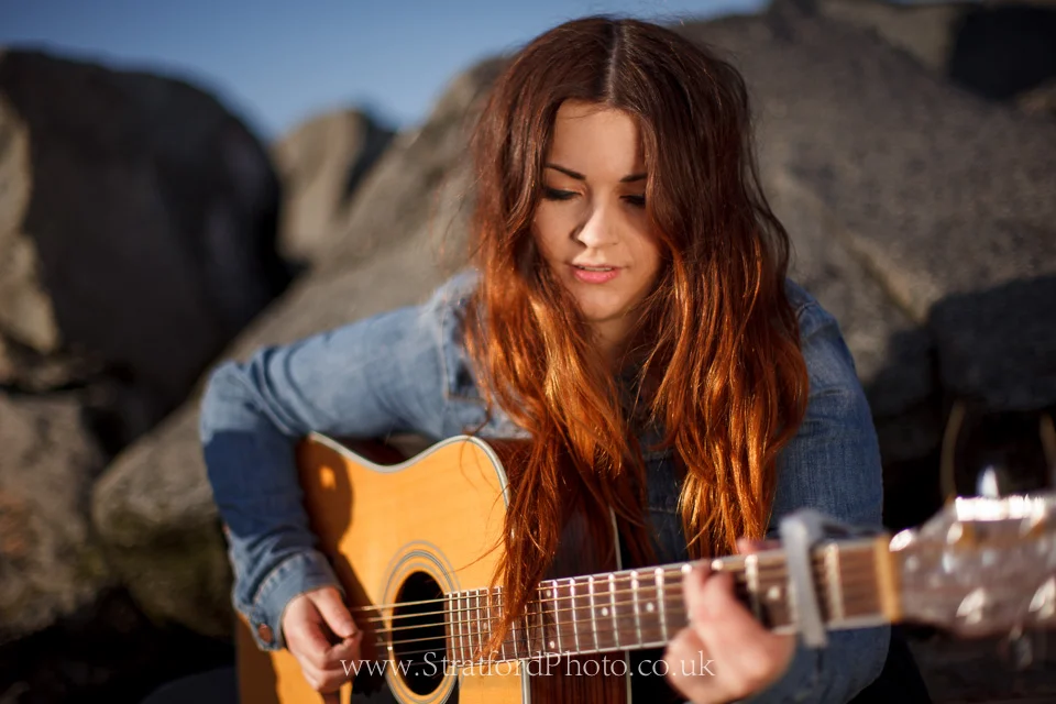 Demi McLeod plays guitar on New Brighton beach.