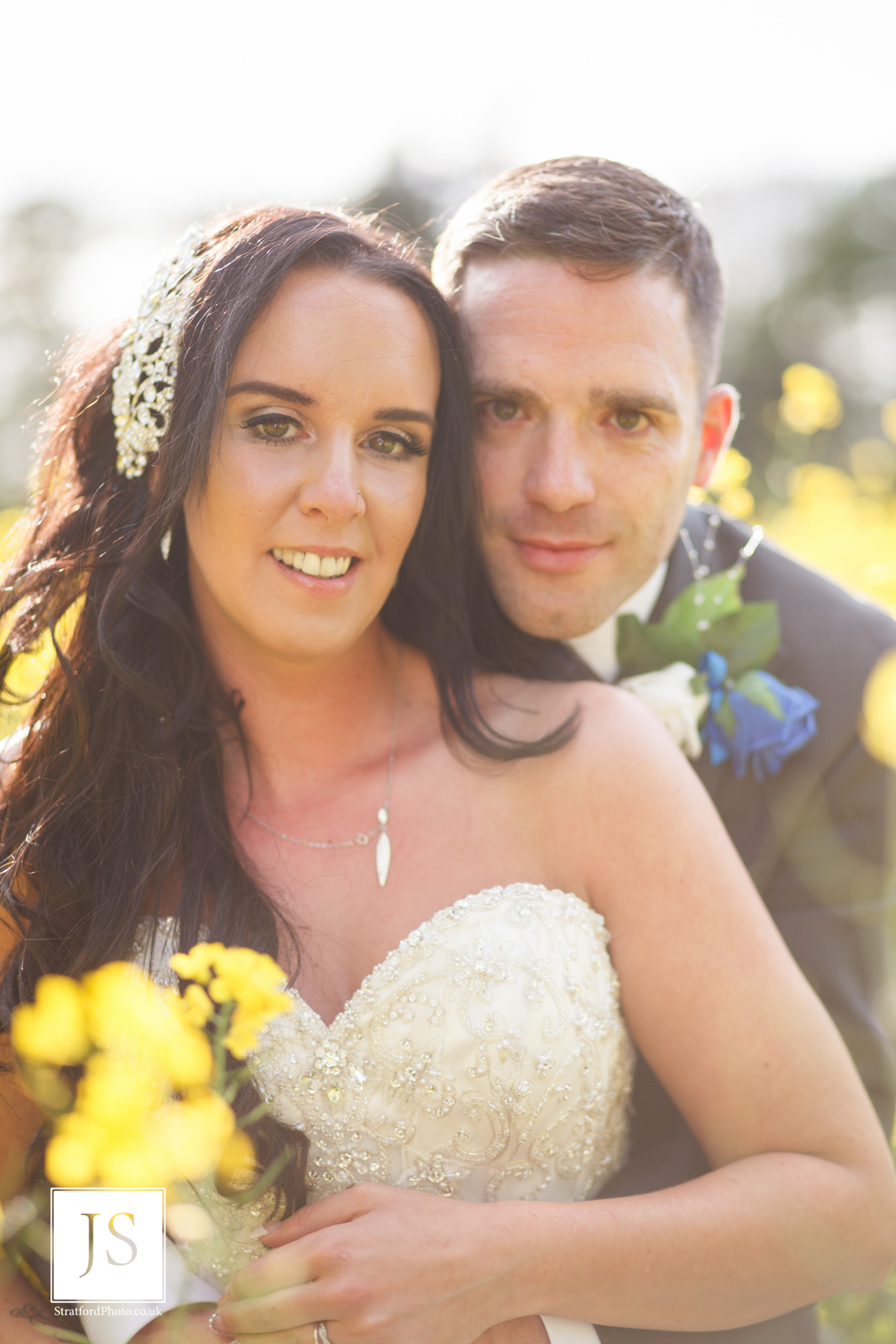 A bride smiles as her groom holds her from behind in a field of yellow rapeseed.jpg