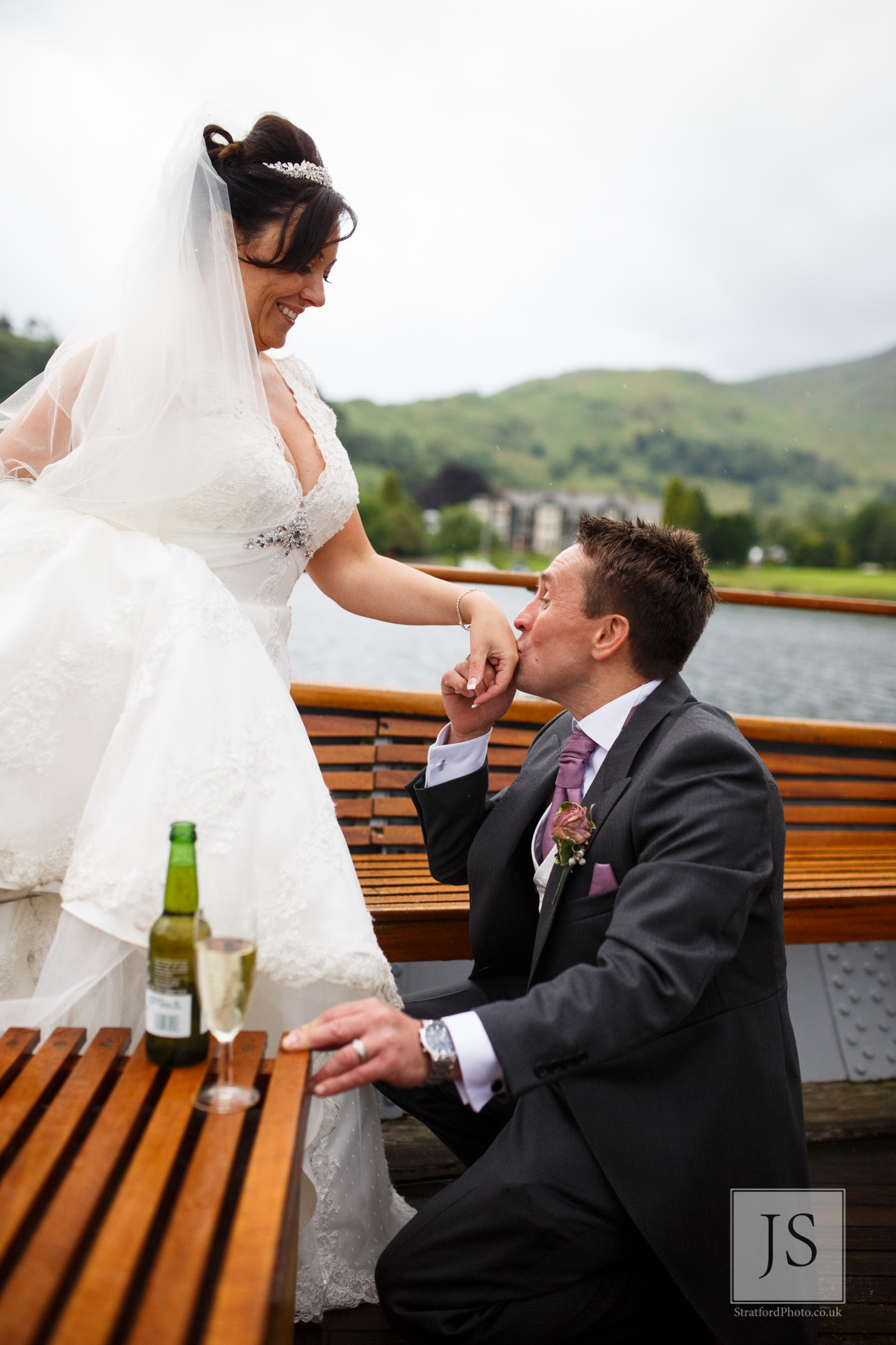 A groom kisses his brides hand at the spot where he proposed on Lake Ullswater.jpg