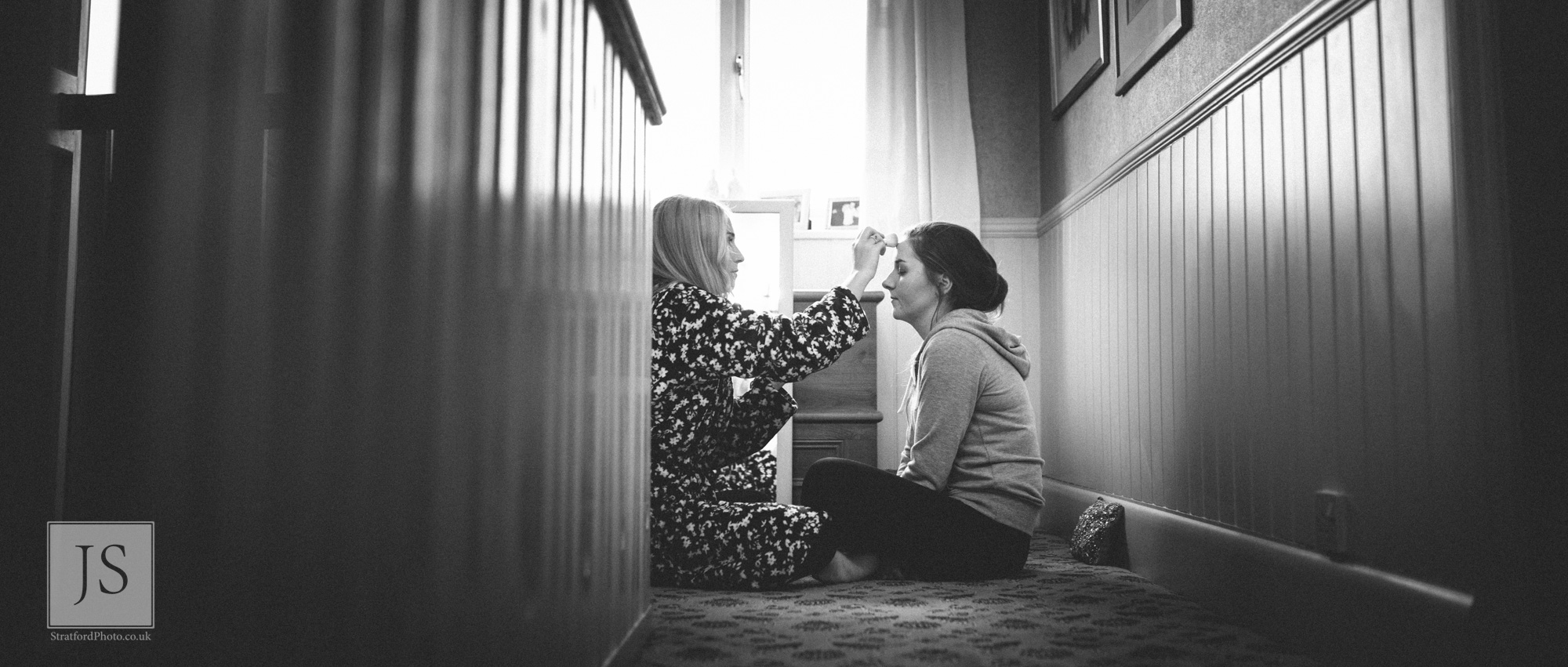 A couple of bridesmaids help each other with makeup.jpg