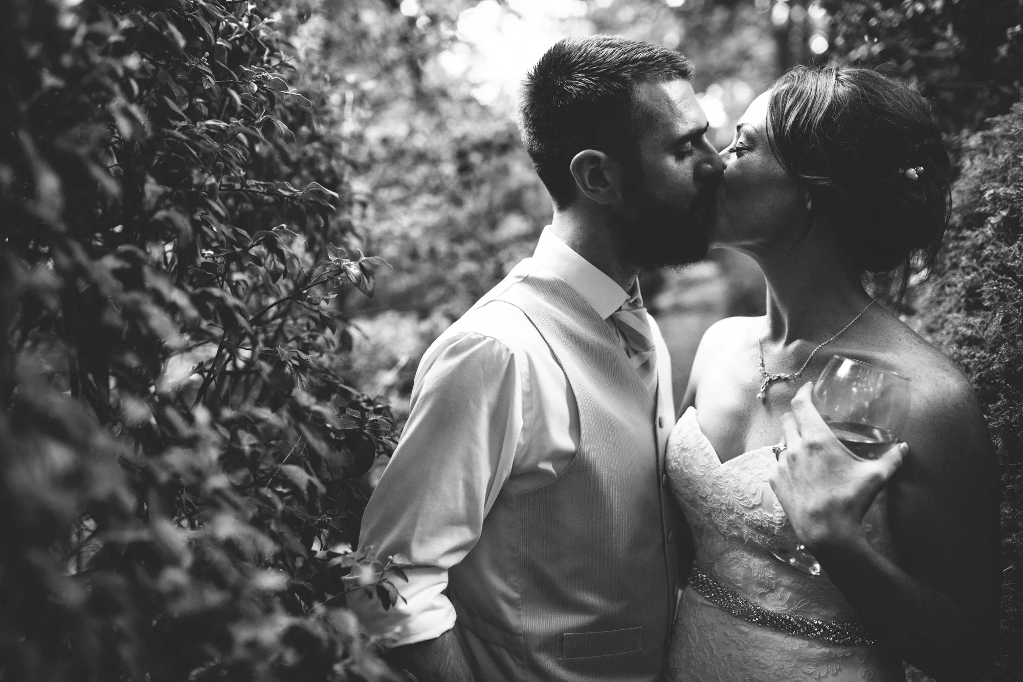 A bride and groom kiss in the privacy of a hedge